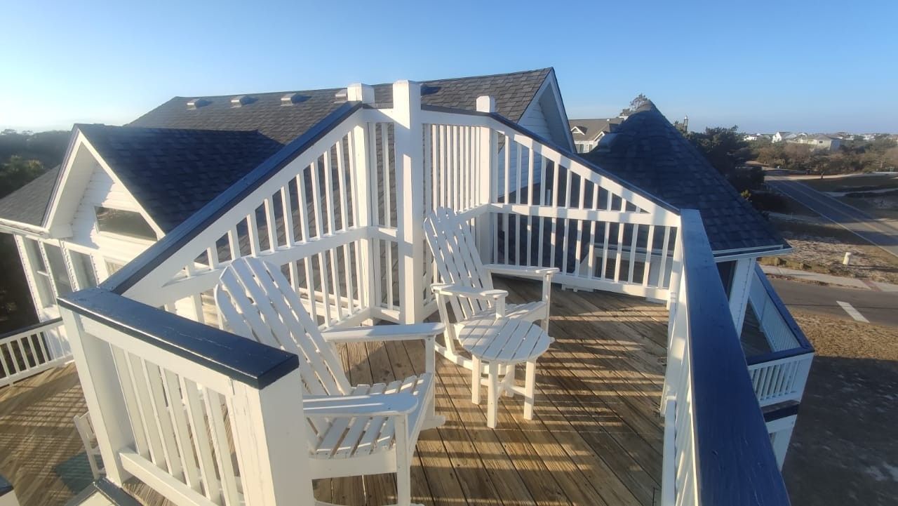 White rooftop deck with Adirondack chairs and striped canopy overlooking the coast at sunset