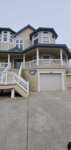Two-story beige house with white trim, front porch, garage, and staircase leading to the entrance