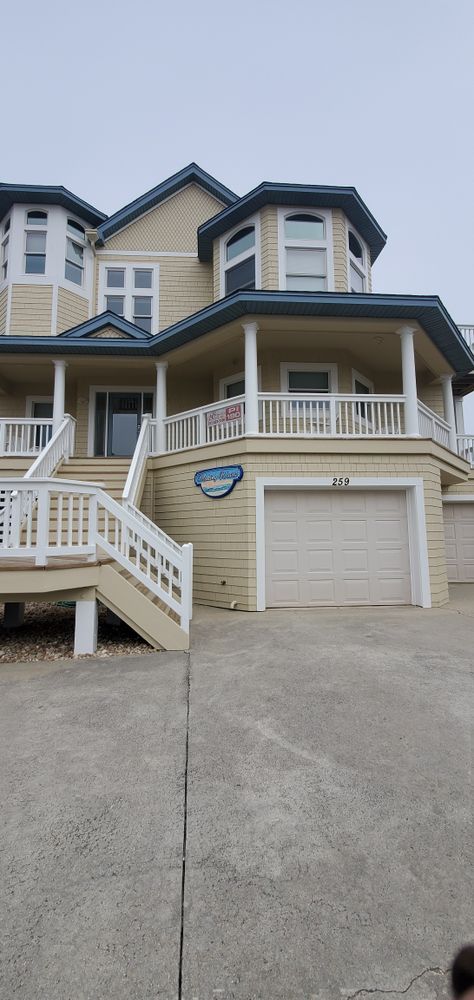 Front view of a beige house with white trim, a covered porch, garage, and front stairs leading up from the driveway.