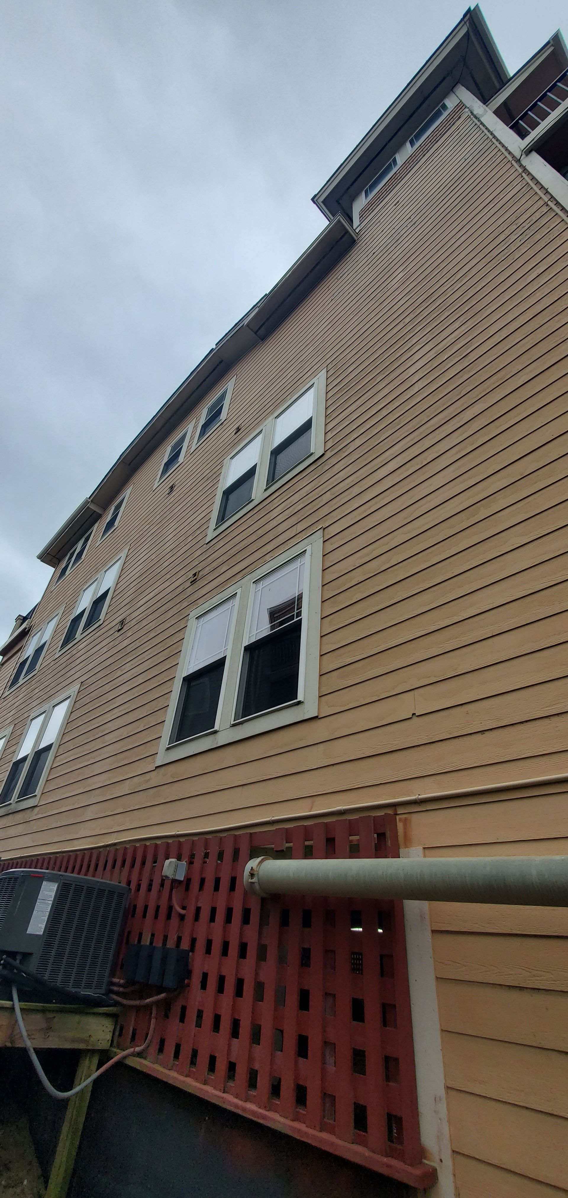 Upward view of a tan brick building with white-trimmed windows and red latticework below