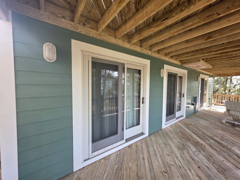 Covered wooden porch with teal siding, white sliding doors, and exposed beam ceiling.