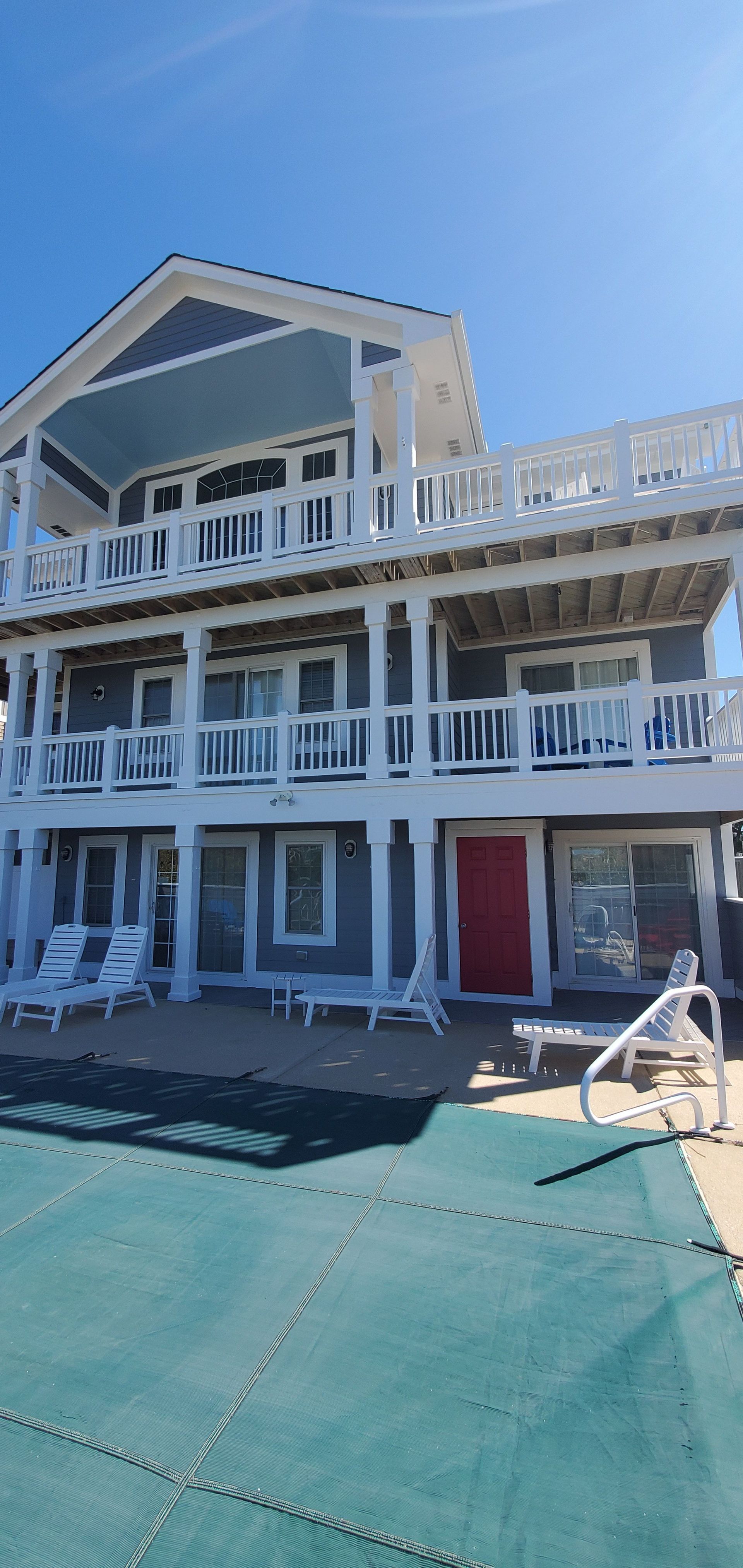 Two-story white beachfront building with balconies and red doors beside a turquoise deck