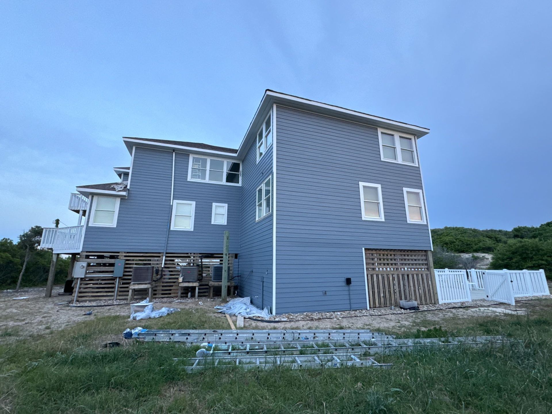Blue-gray house under construction with unfinished deck and lawn in front.