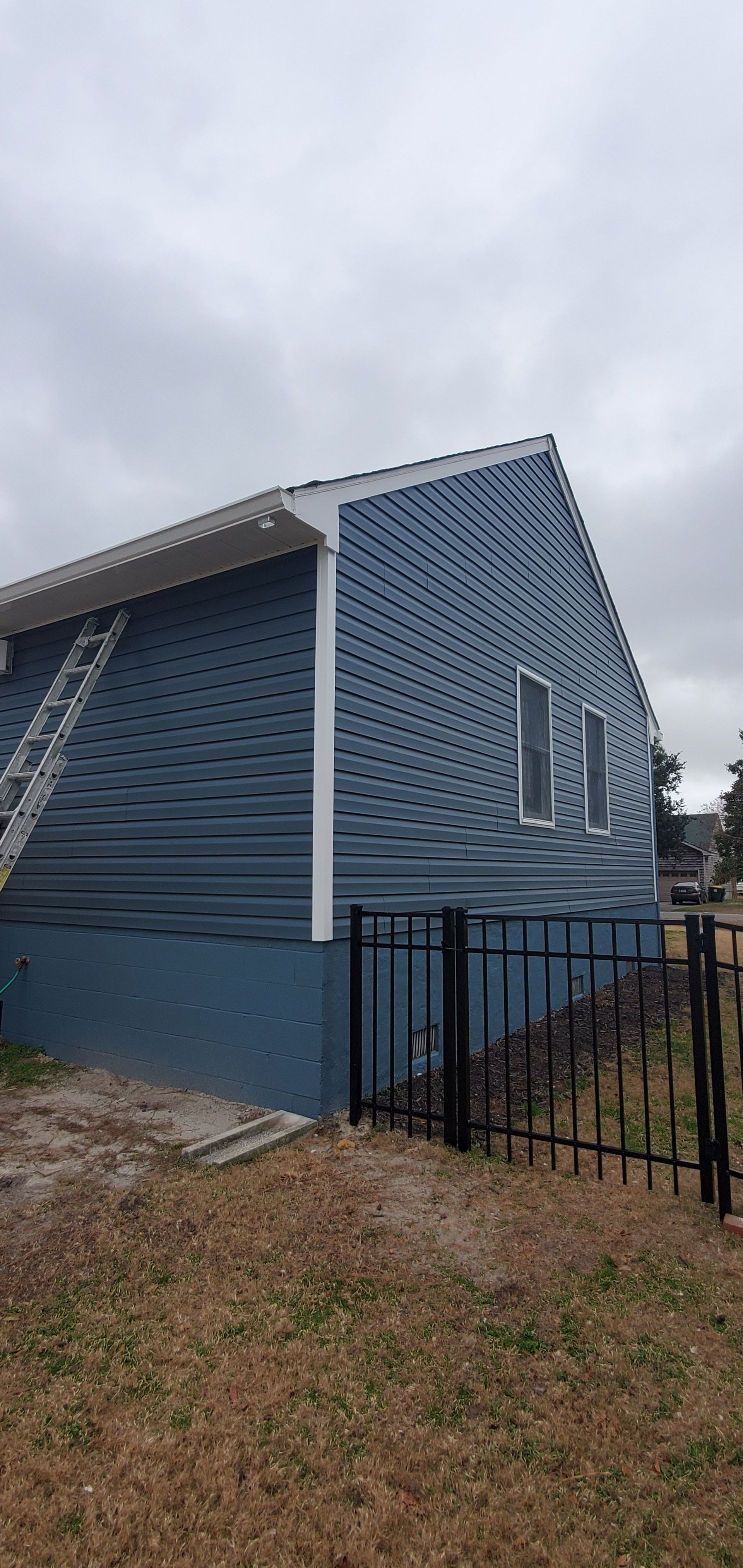 Blue house exterior with angled roof, white trim, and a black metal fence in front