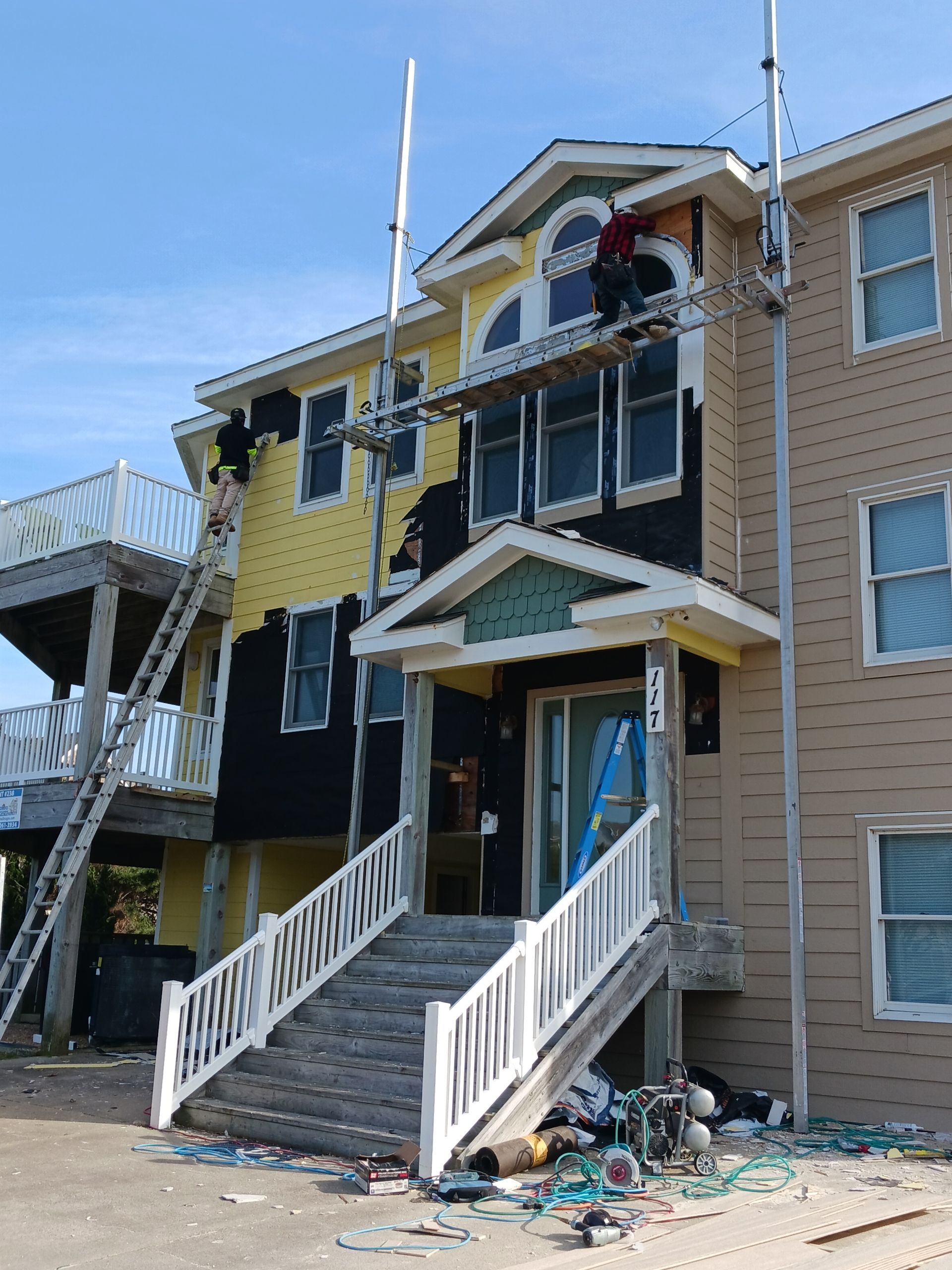 Damaged yellow-and-blue house with collapsed stairs and debris scattered on the ground