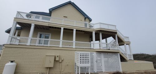 Two-story beige seaside house with white railings and deck on a cloudy day