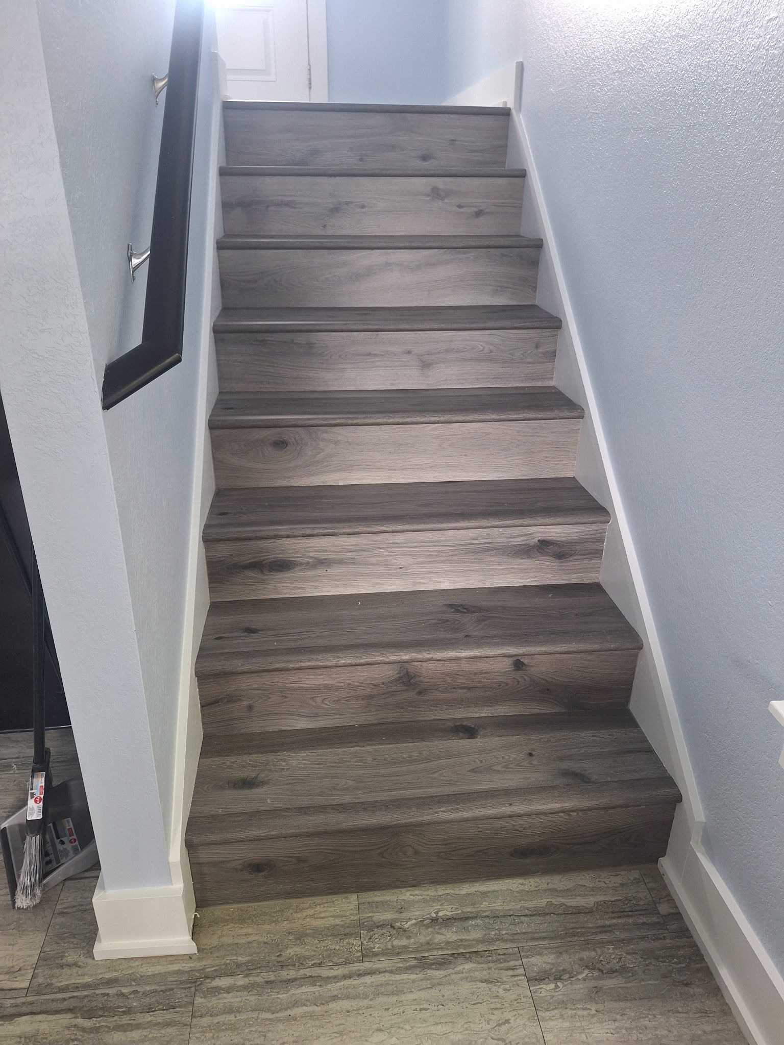 Indoor staircase with gray wood steps, white walls, and a black handrail.