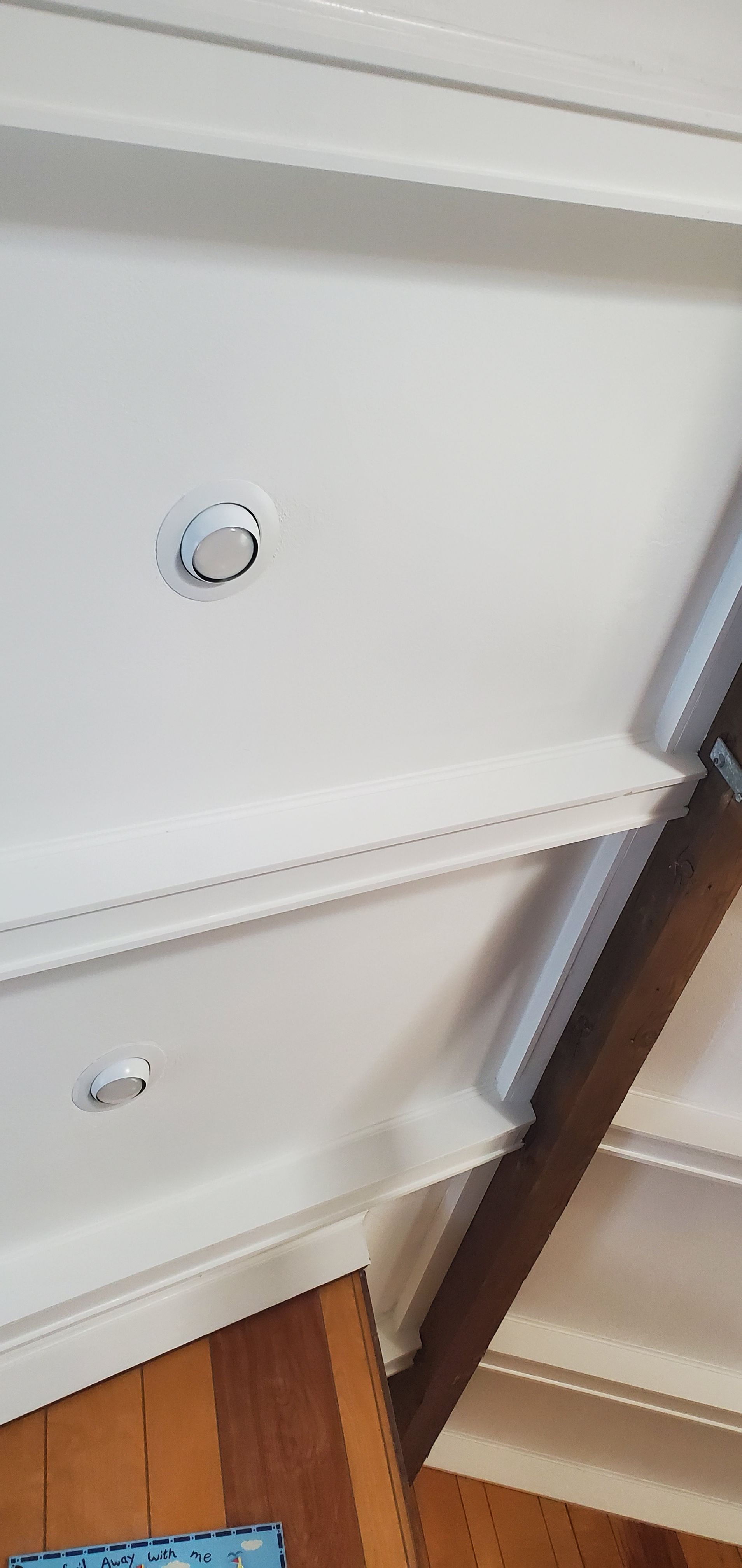 White built-in shelving with a dark wooden frame and a small circular fixture on the back panel, viewed close up