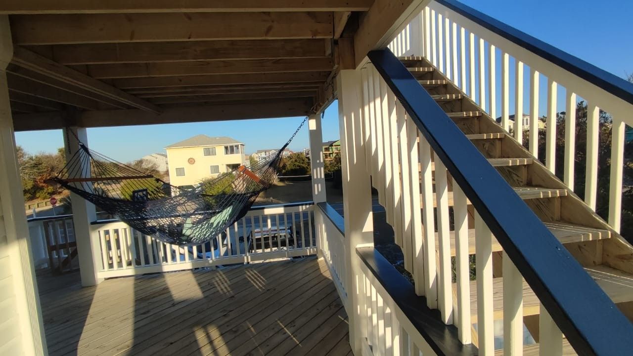 Covered outdoor staircase with white railings and blue trim overlooking a sunlit residential area.