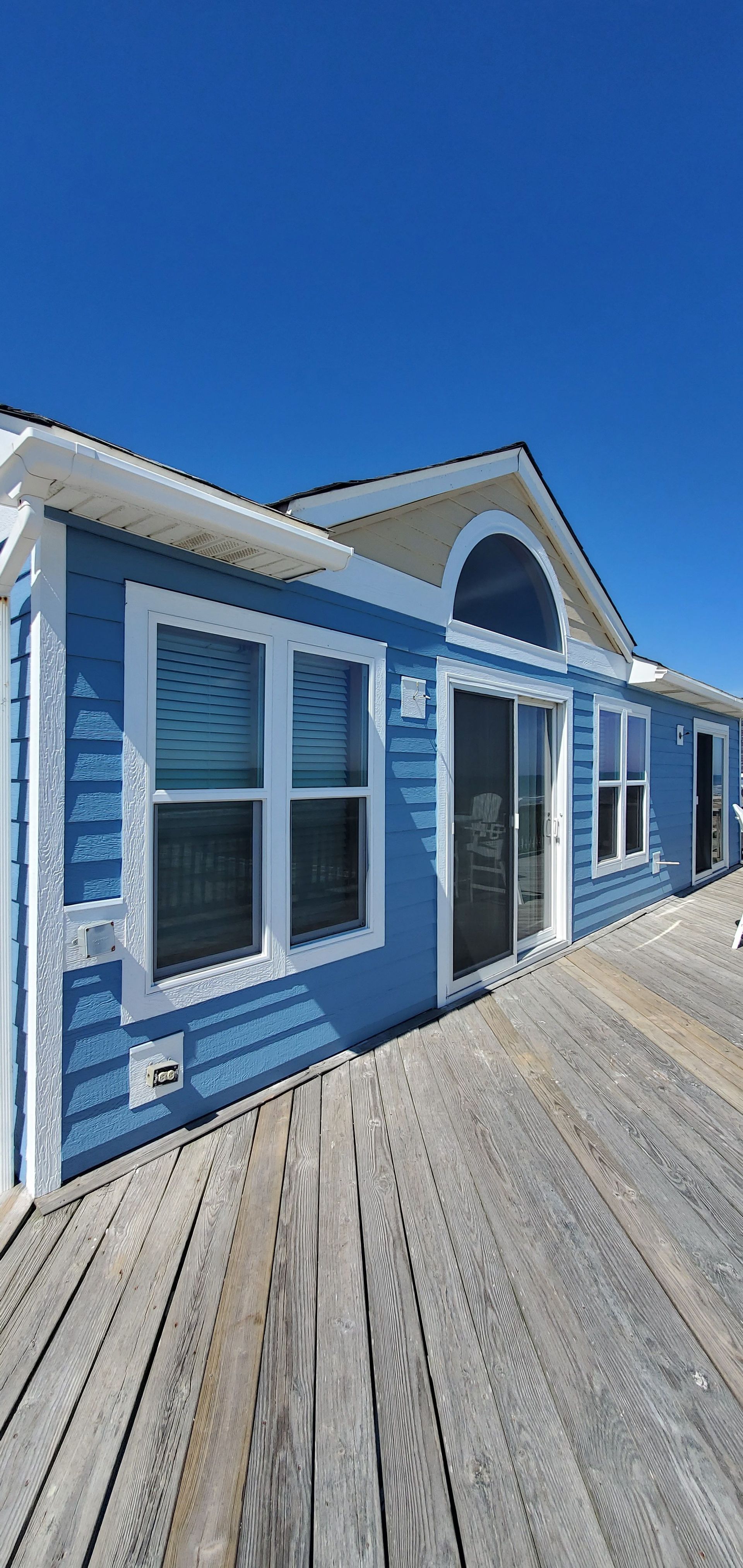 Blue beachside building with white trim and arched windows beside a wooden boardwalk under a clear sky