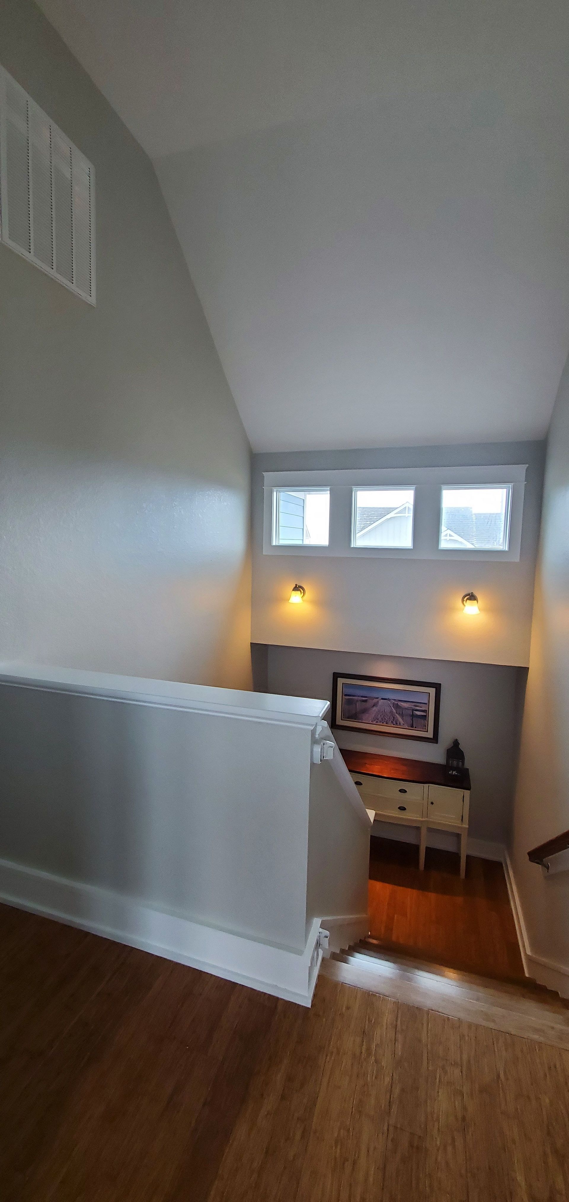 Staircase landing with white walls, hardwood floors, windows, and a view down to a lit room below