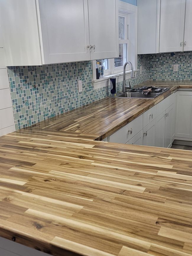Modern kitchen with white cabinets, mosaic tile backsplash, and a butcher-block countertop run