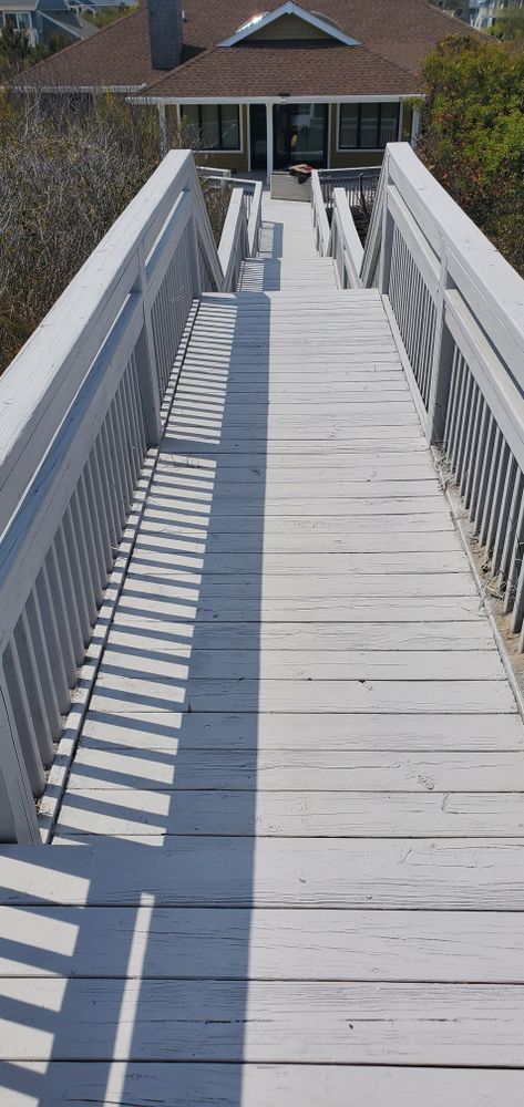 White wooden ramp with railings leading down to a house entrance in bright sunlight