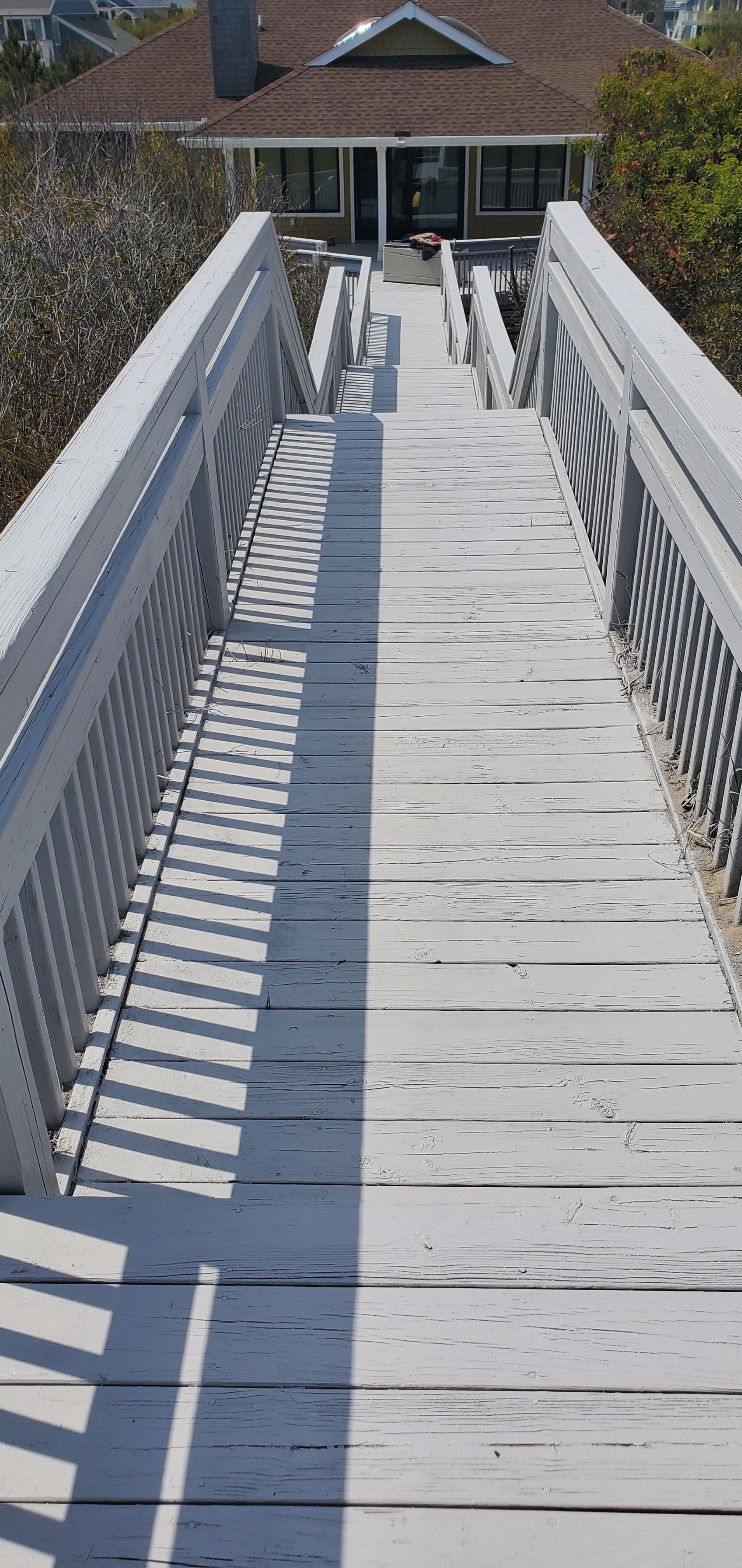 White wooden ramp with railings leading to a building entrance in bright sunlight
