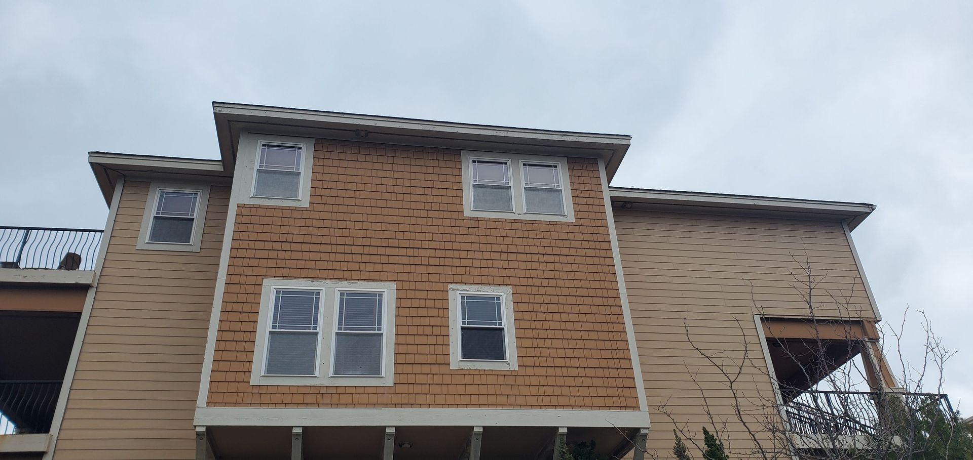 Brick townhouse exterior with beige siding, multiple windows, and a small balcony under an overcast sky