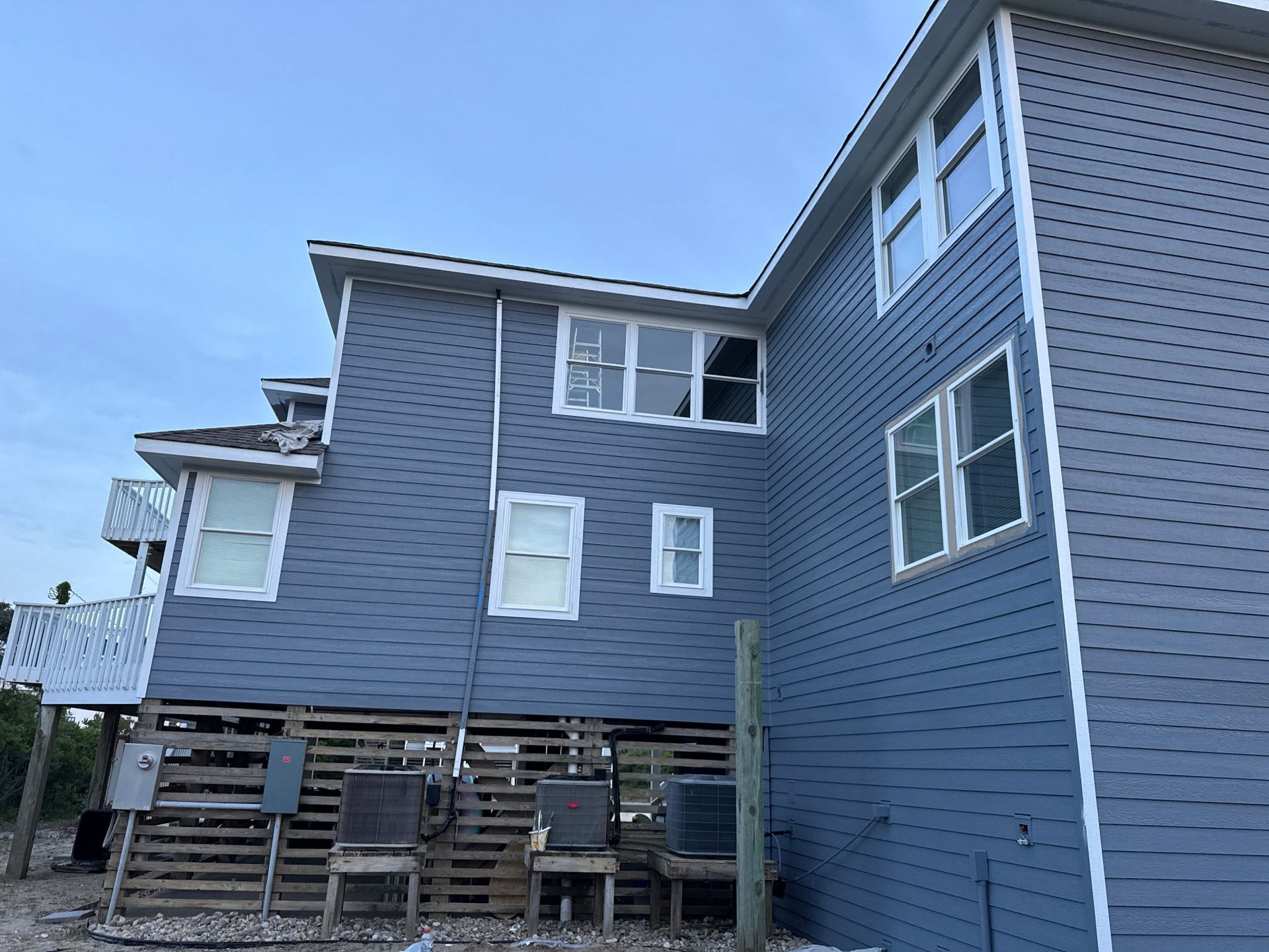 Blue-gray house with raised deck and patio chairs under a clear sky