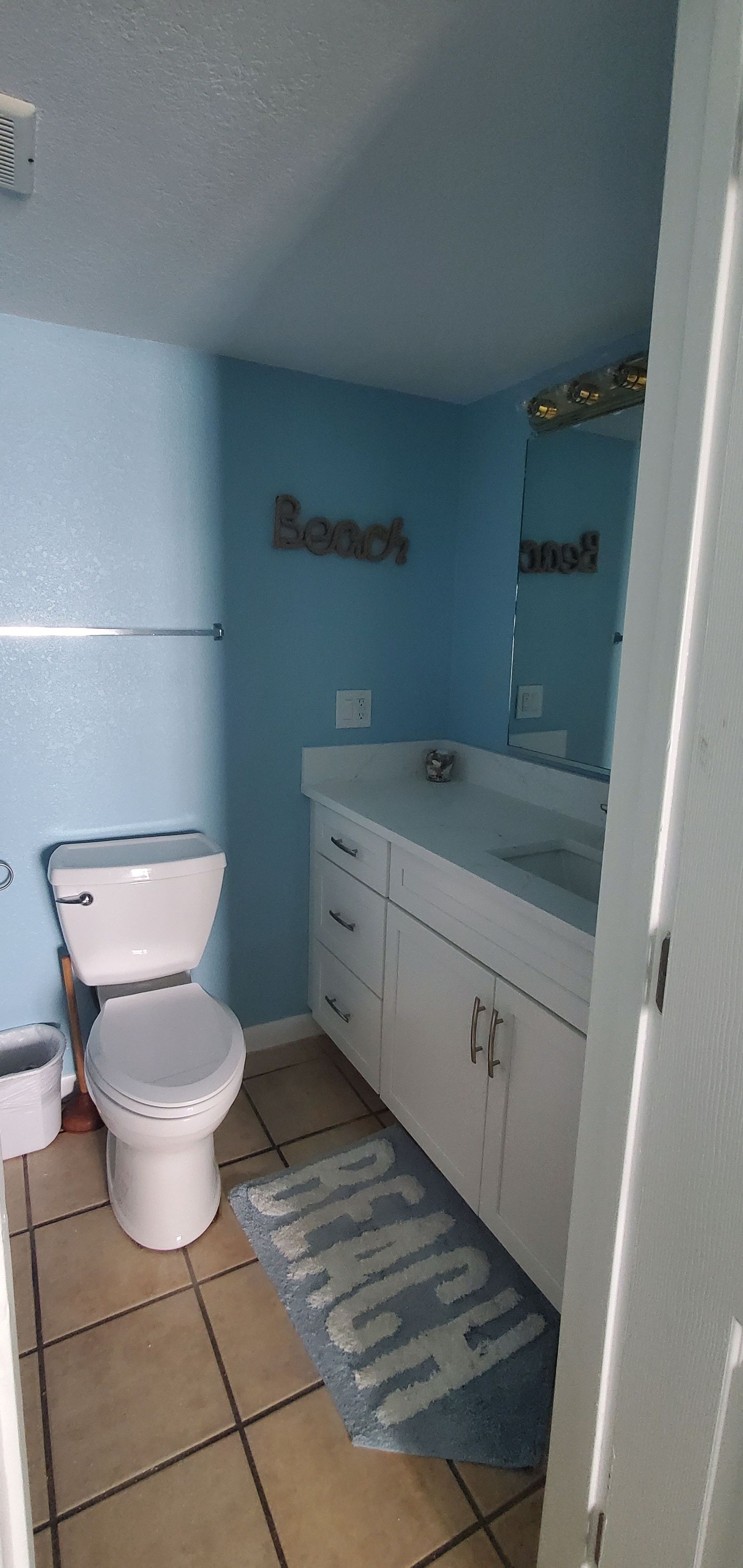 Small bathroom with a toilet, vanity, blue walls, and a striped rug.