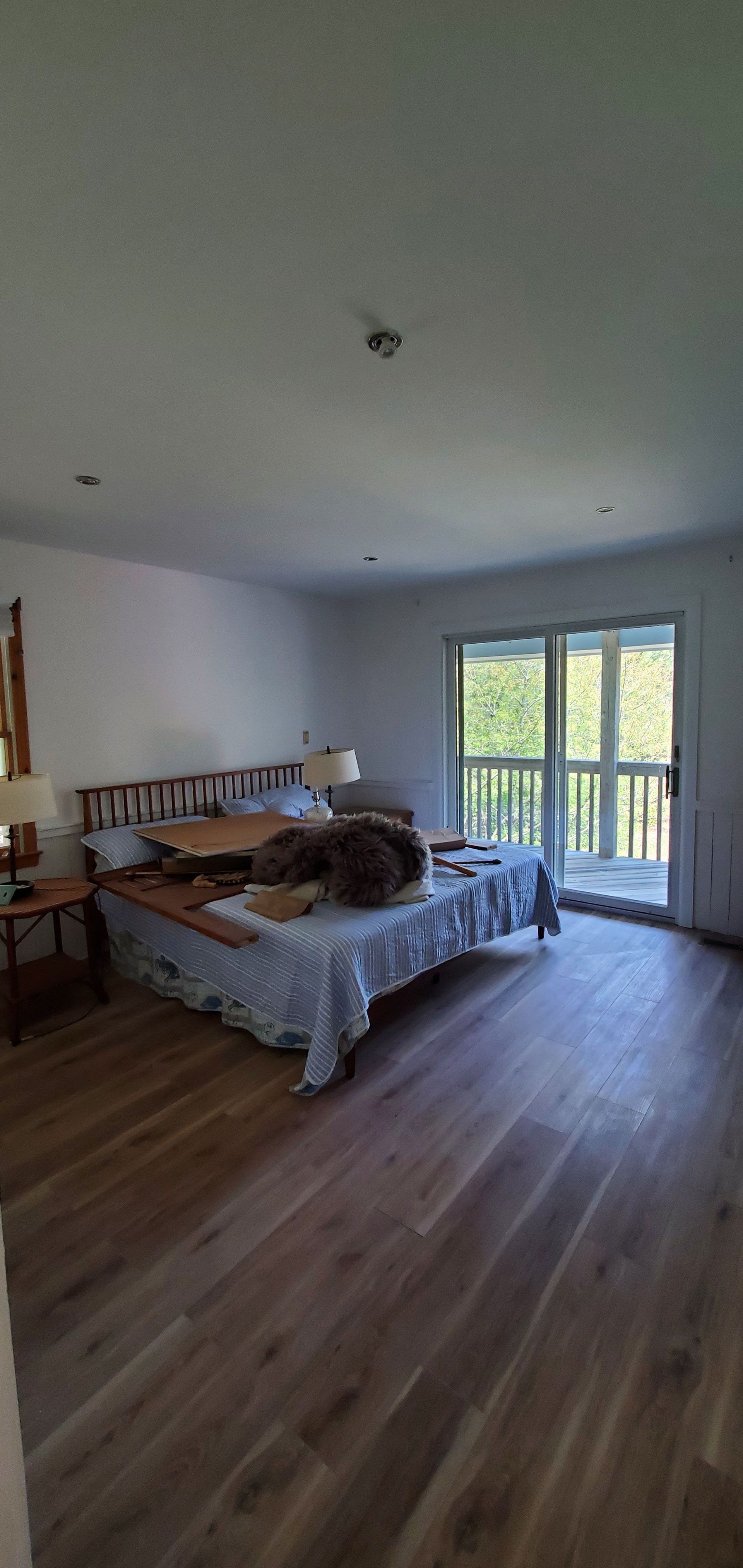 Bright bedroom with a bed, wood floors, white walls, and balcony doors letting in daylight.
