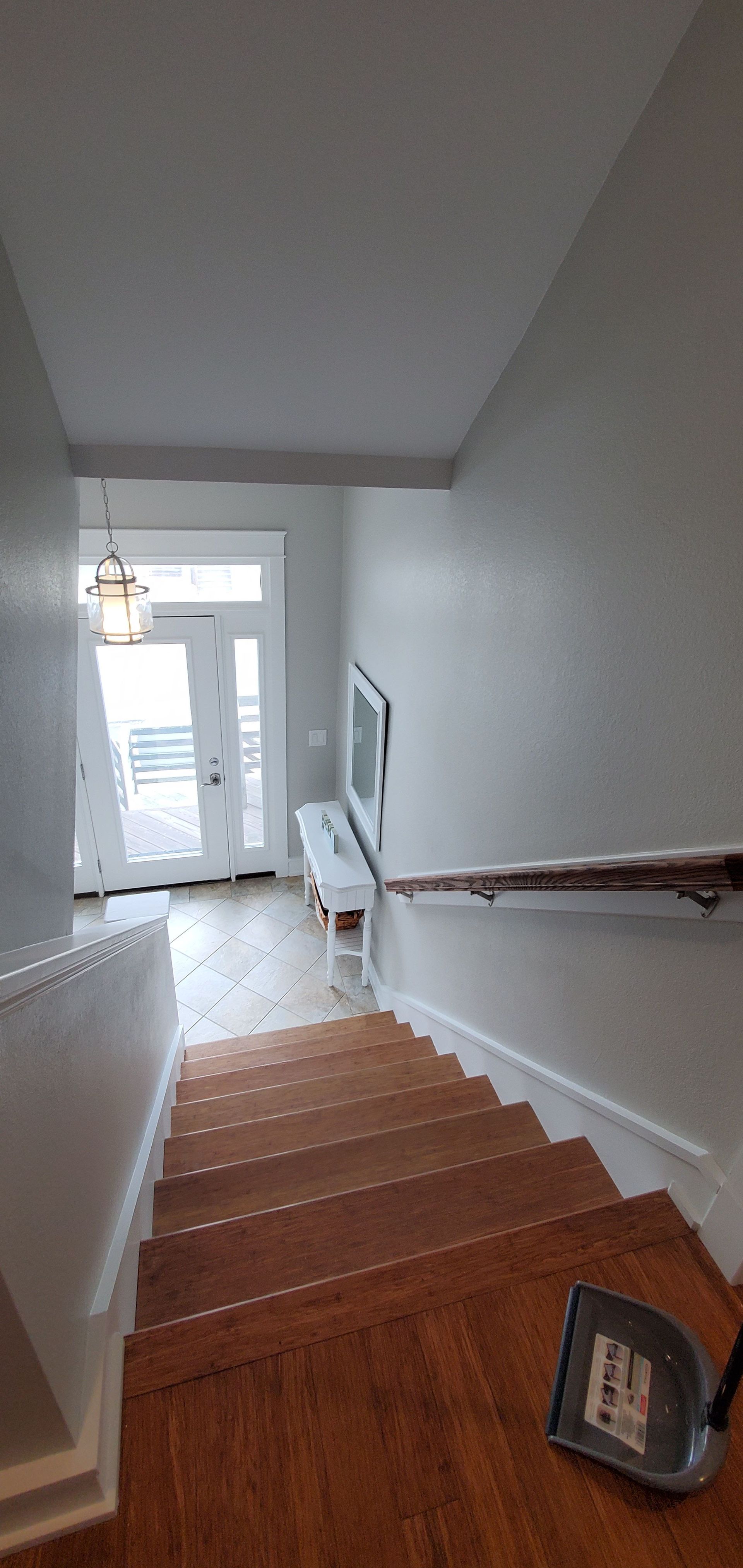 Staircase view toward a bright entryway with hardwood steps, white walls, and a hanging light fixture.