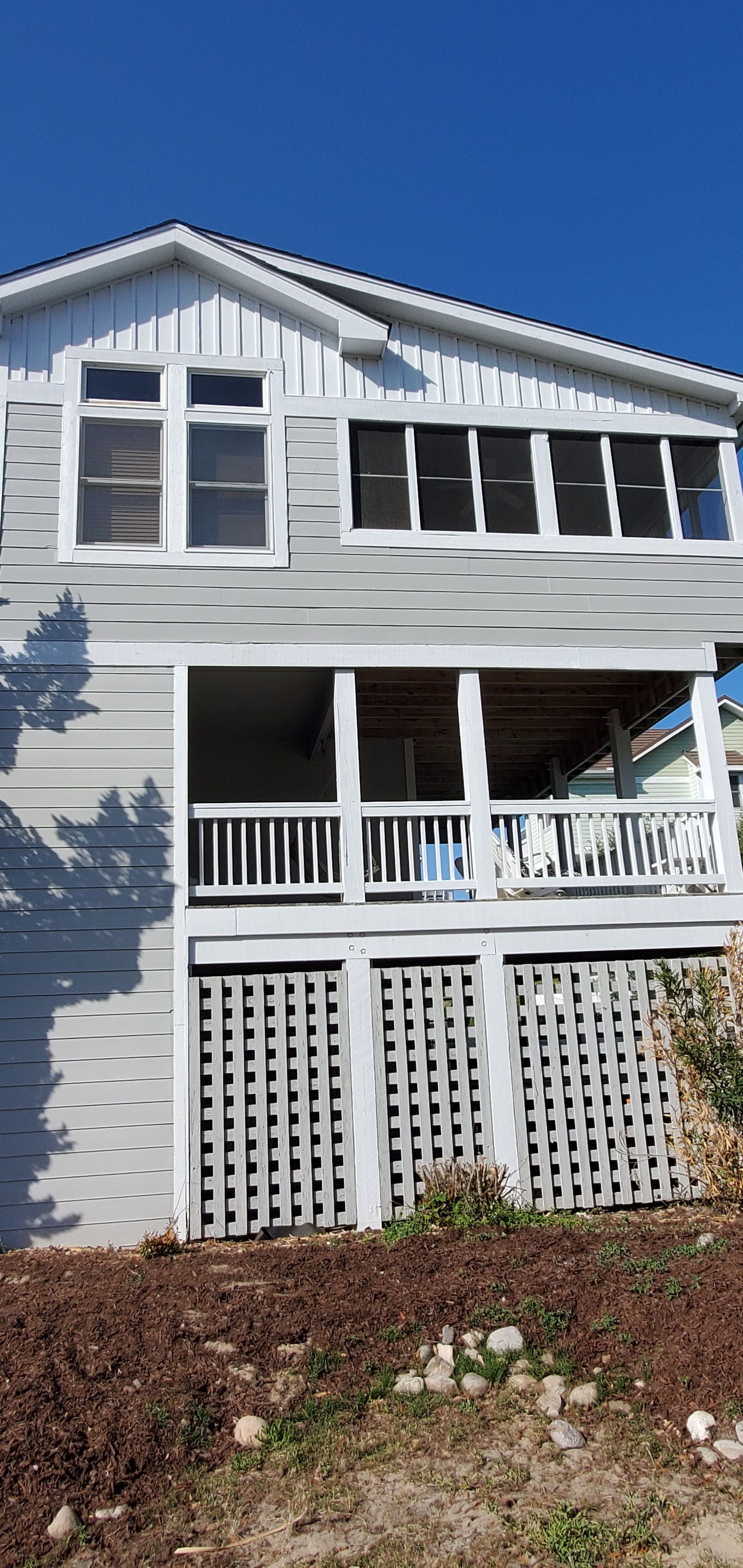 White house with blue shutters, front porch, and lattice skirting under a clear blue sky.