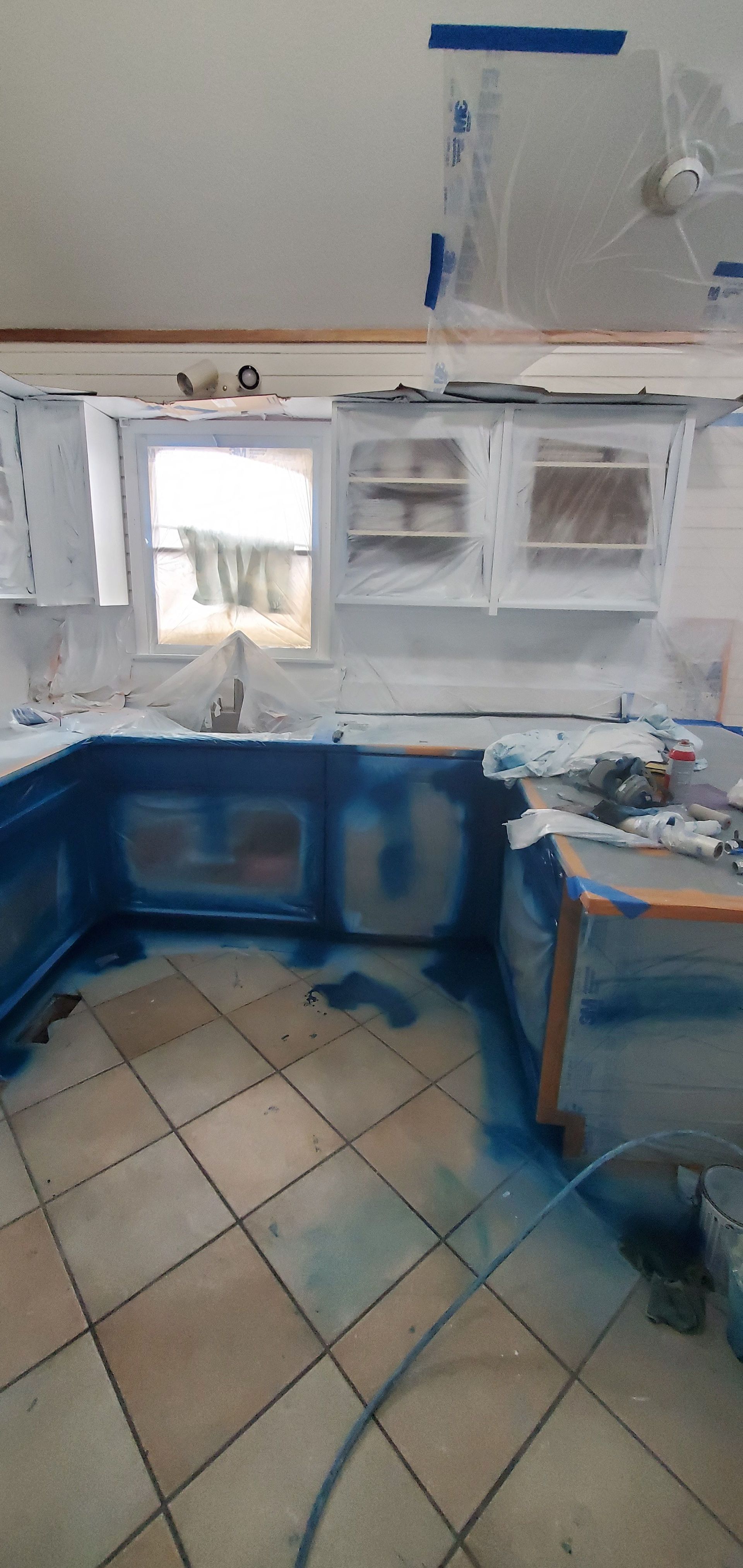 Small kitchen with blue cabinets, white shelves, tiled floor, and a sink under a window.