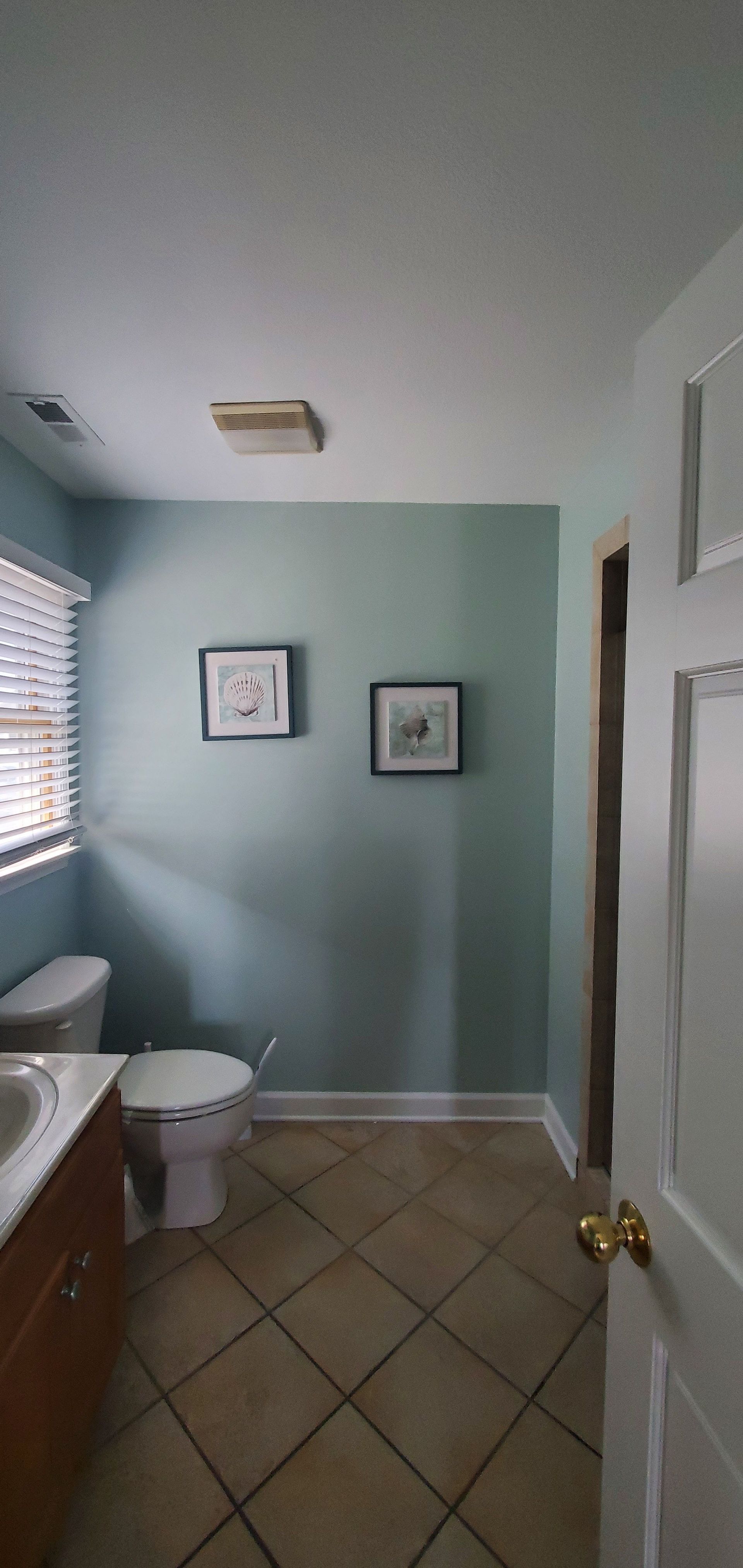 Small bathroom with mint walls, tiled floor, sink, toilet, window, and framed wall art.