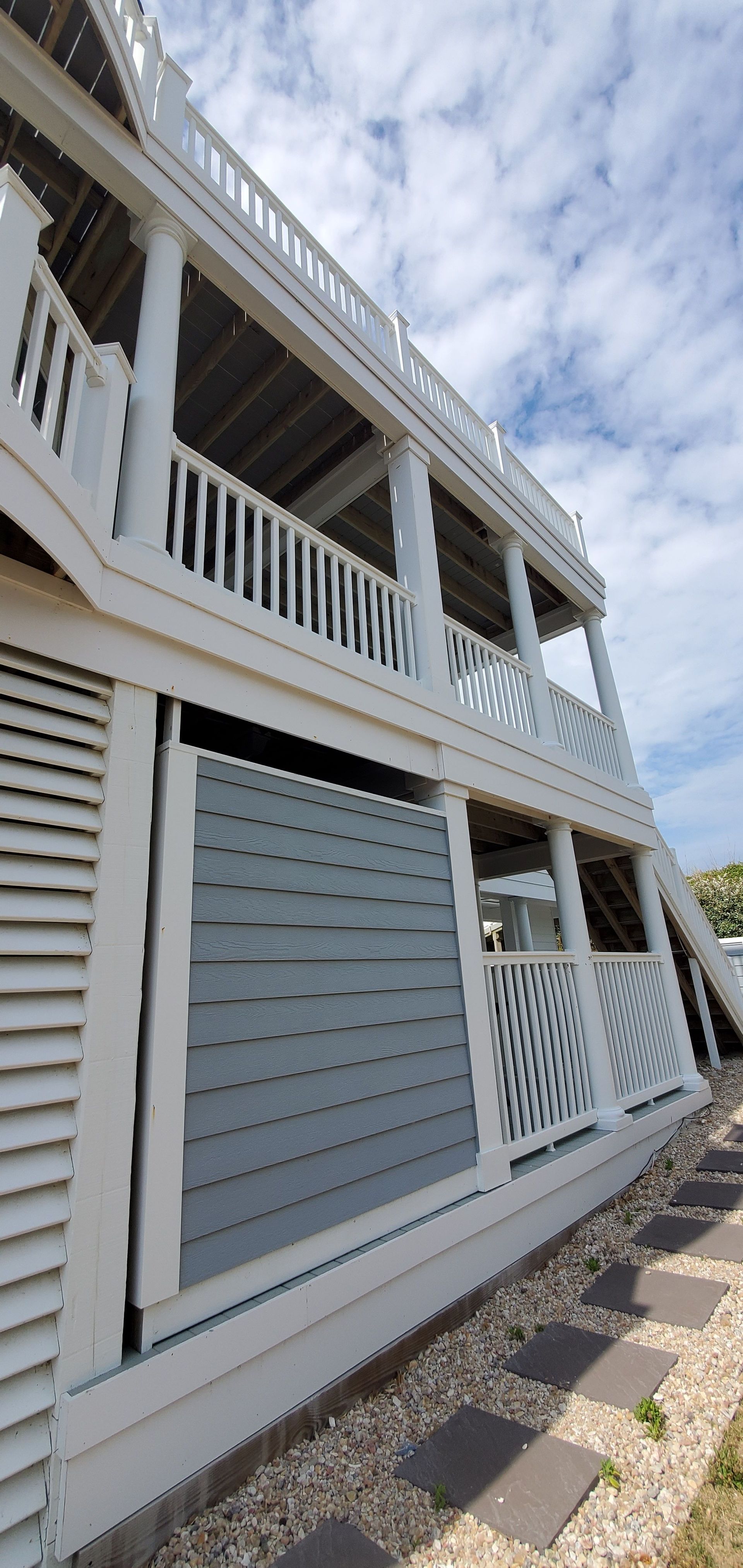 White beach house exterior with balconies, railings, and gray shutters under a partly cloudy sky
