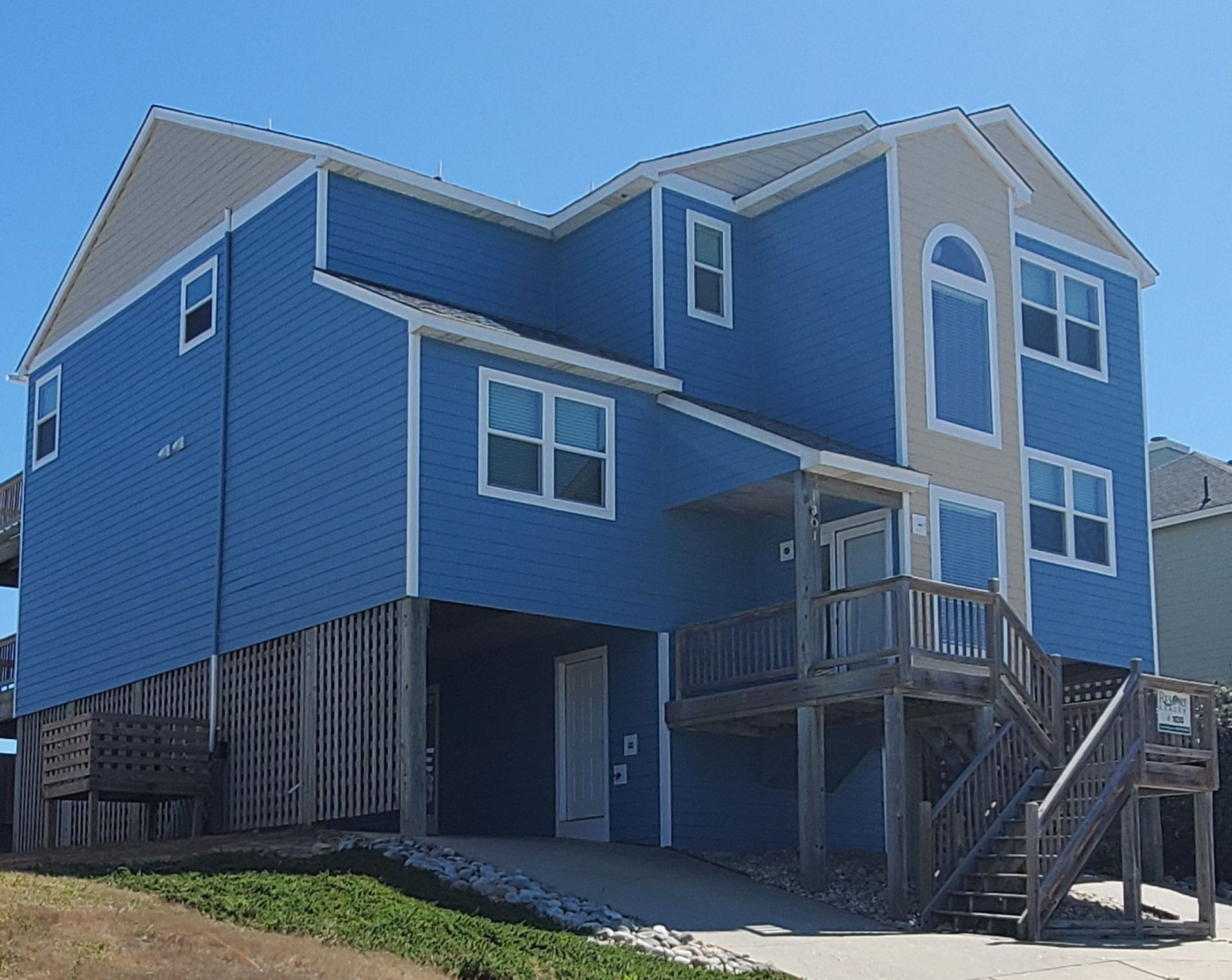 Blue two-story house with white trim and front porch, seen from the side on a sunny day