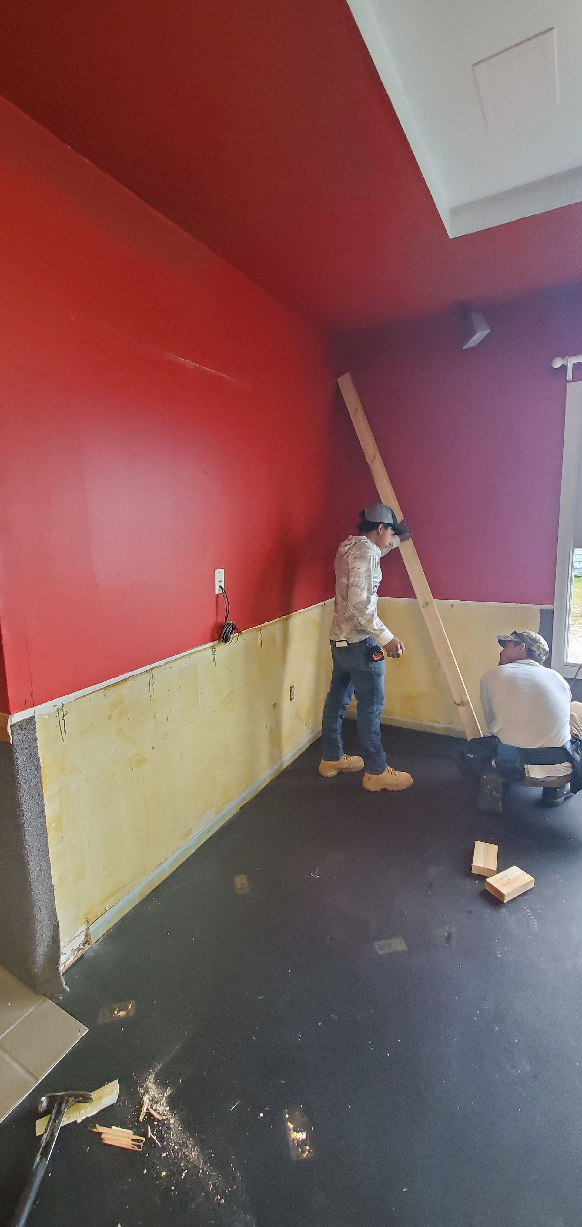 Two people painting a red room, one on a ladder and one kneeling near the wall.