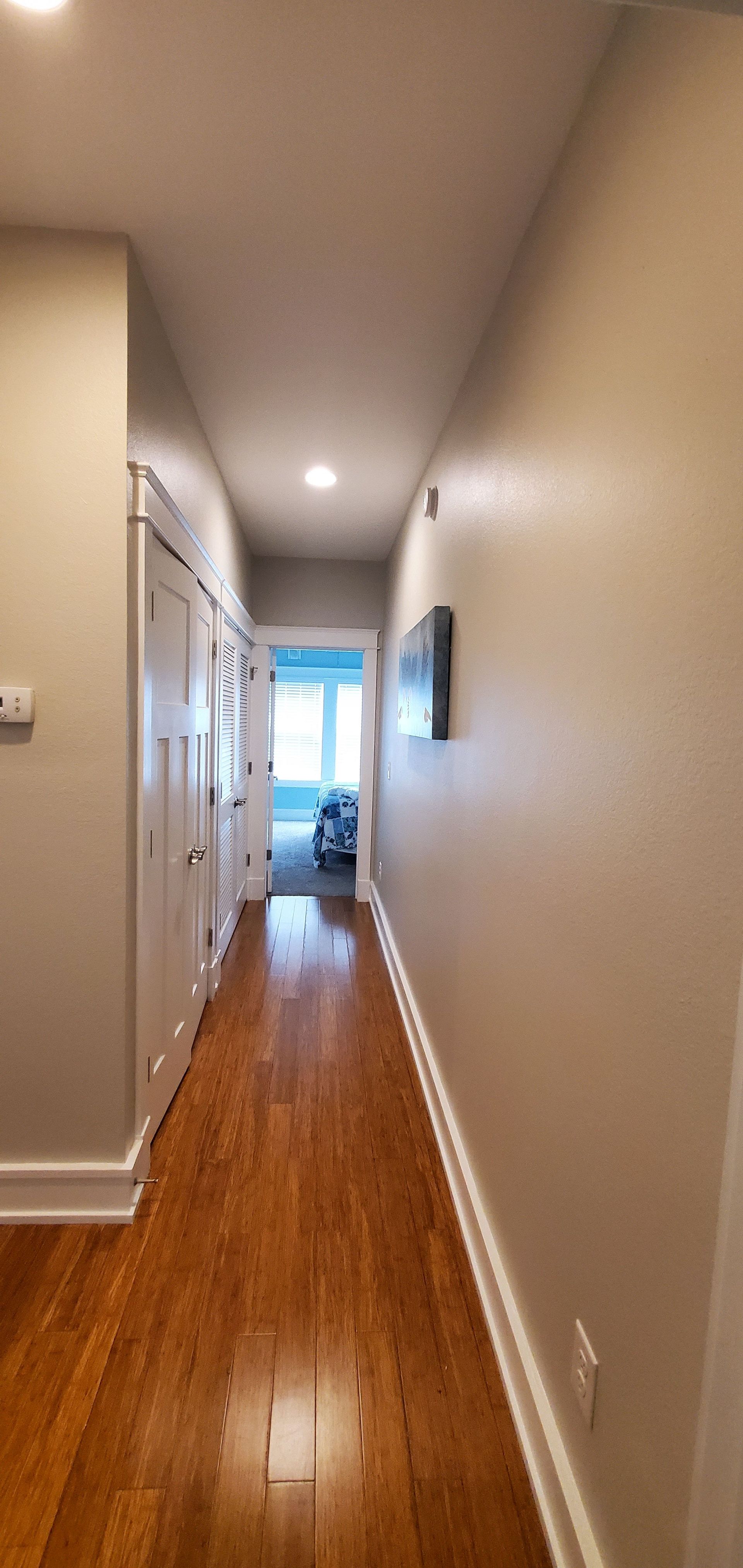 Long hallway with hardwood floors, beige walls, and a bright window at the far end