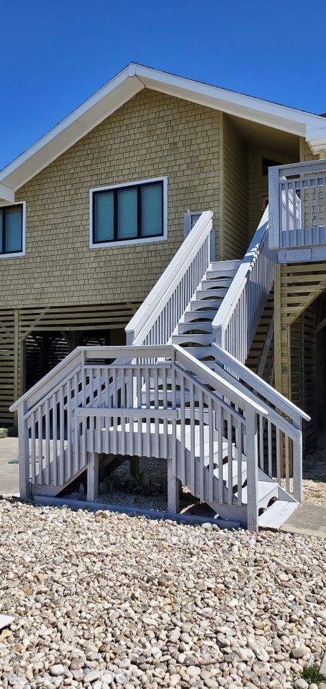 White house exterior with elevated deck, stairs, and gravel yard under a clear blue sky