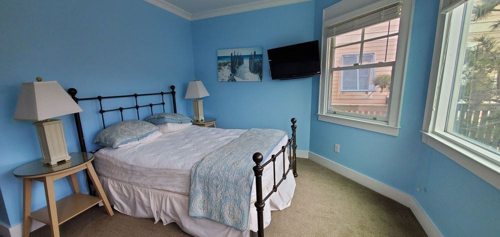 Blue bedroom with black metal bed, white bedding, two lamps, and a window with sunlight