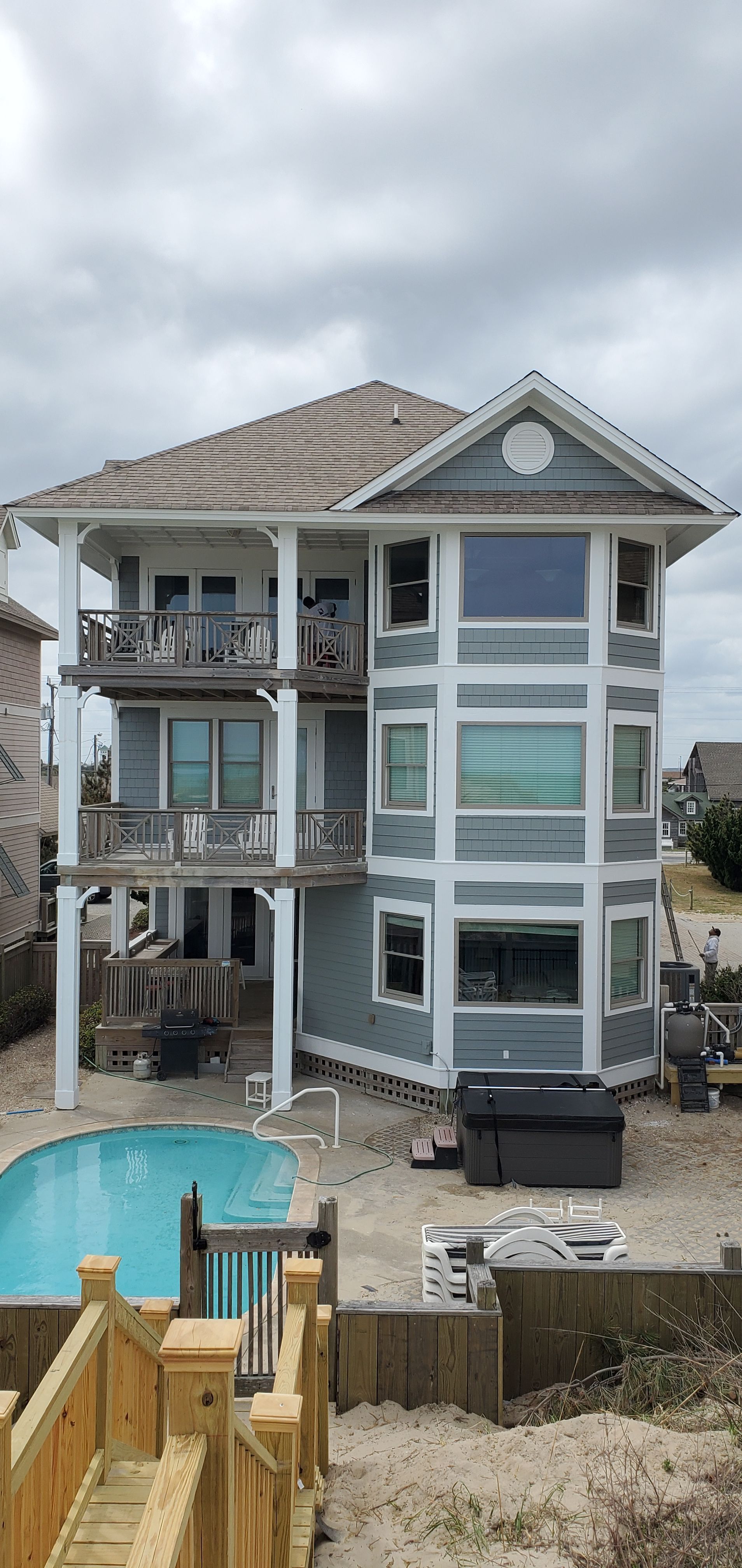 Three-story coastal house under construction beside a swimming pool and wooden deck