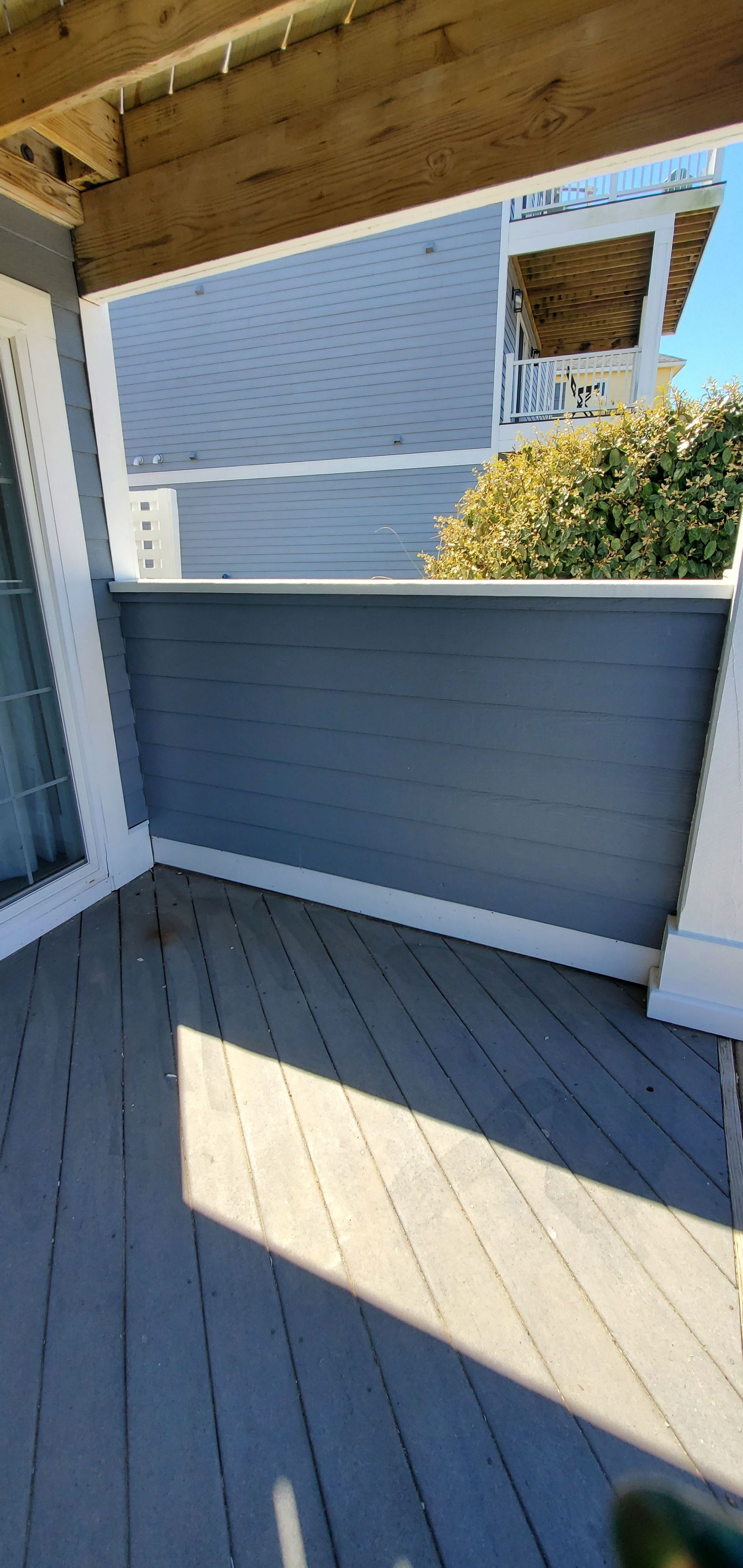 Covered gray deck with white railings and blue house siding, viewed from a corner.