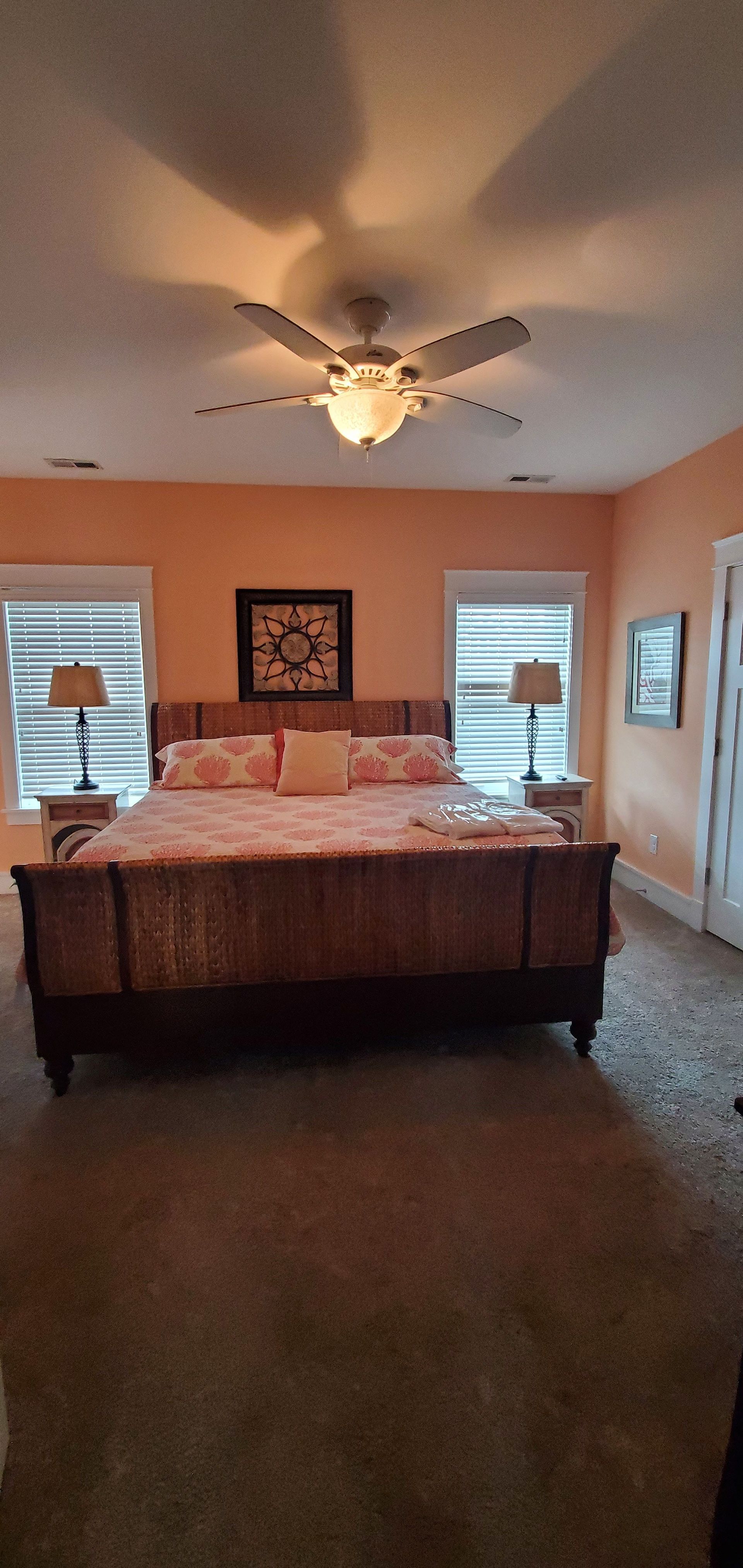 Bedroom with a wooden bed, carpeted floor, ceiling fan, and two windows with blinds.