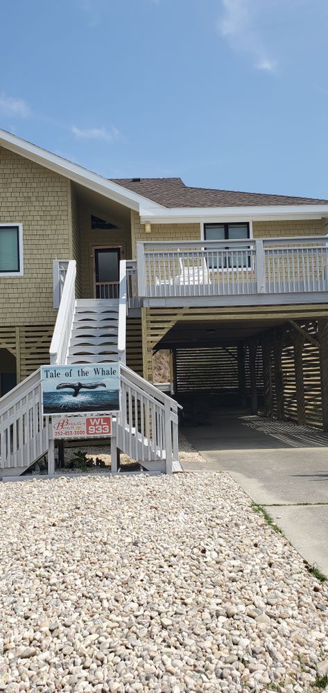 House with raised deck, stairs, and a carport over a gravel driveway under a blue sky