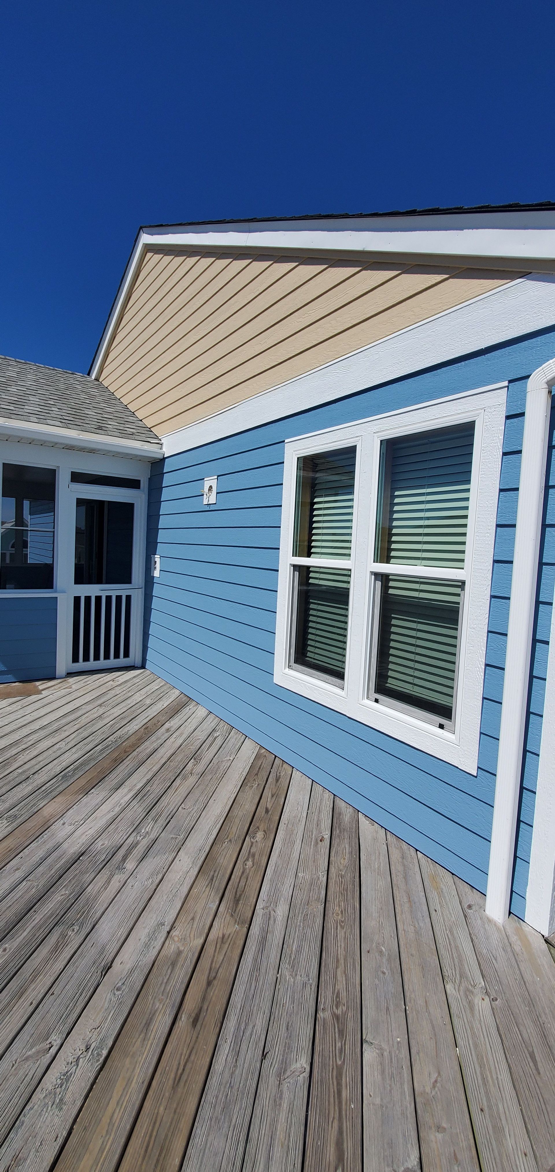 Blue house exterior with white-trimmed windows and a wooden deck under a clear sky