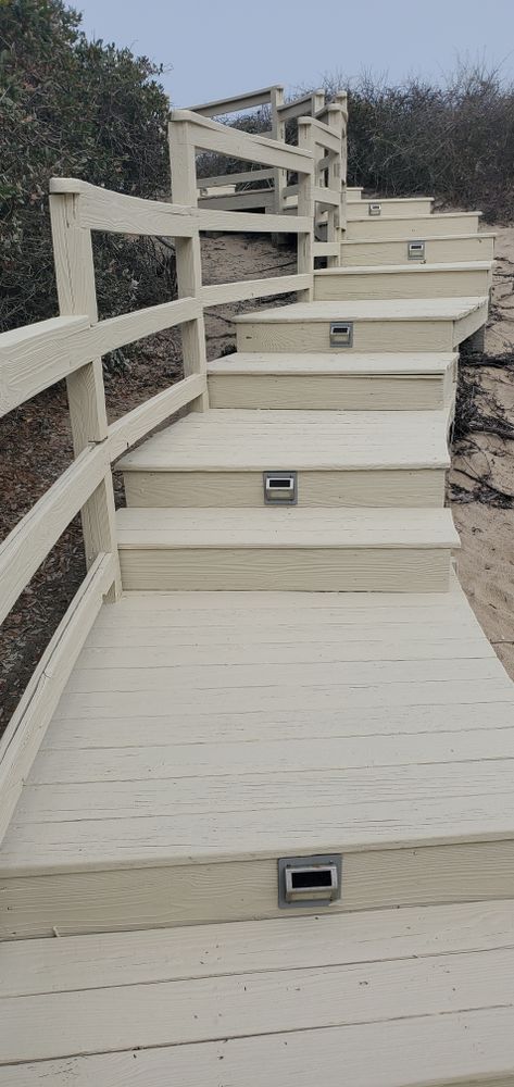 Steep outdoor staircase with beige steps and white railings on a rocky hillside