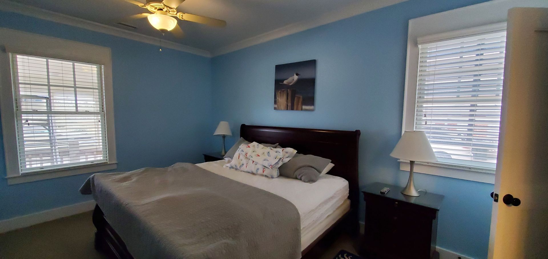 Blue bedroom with a bed, nightstands, windows with blinds, and a ceiling fan