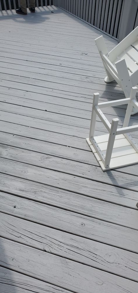Gray wooden deck with white patio chairs and railing in bright sunlight
