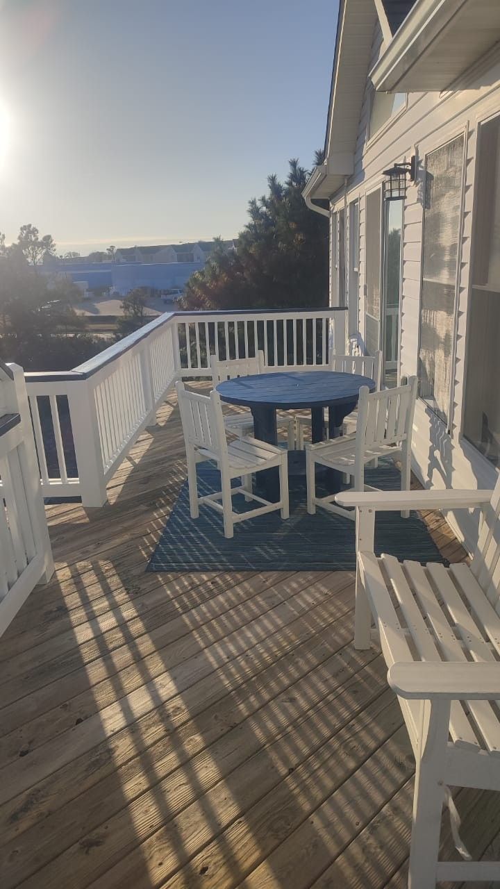 White deck with railing, table and chairs, beside a house overlooking water at sunset