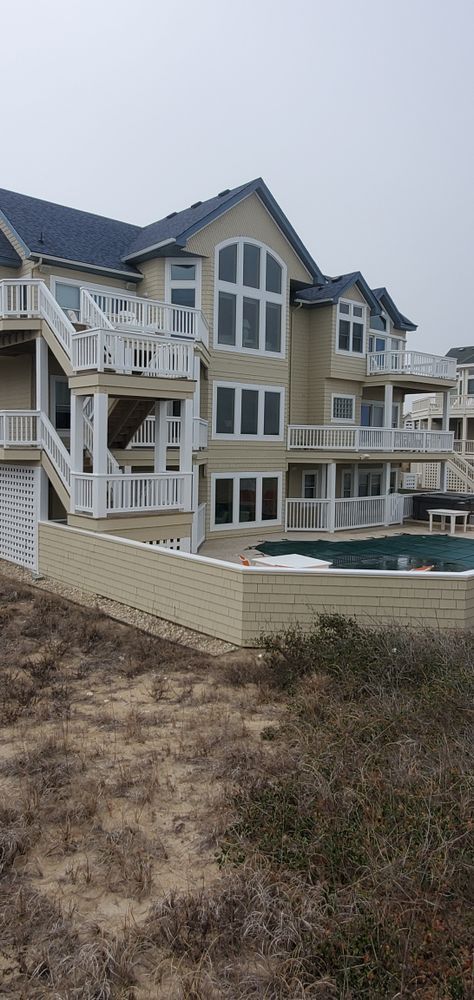 Coastal townhouse with white and beige balconies, pool, and dune grass in front