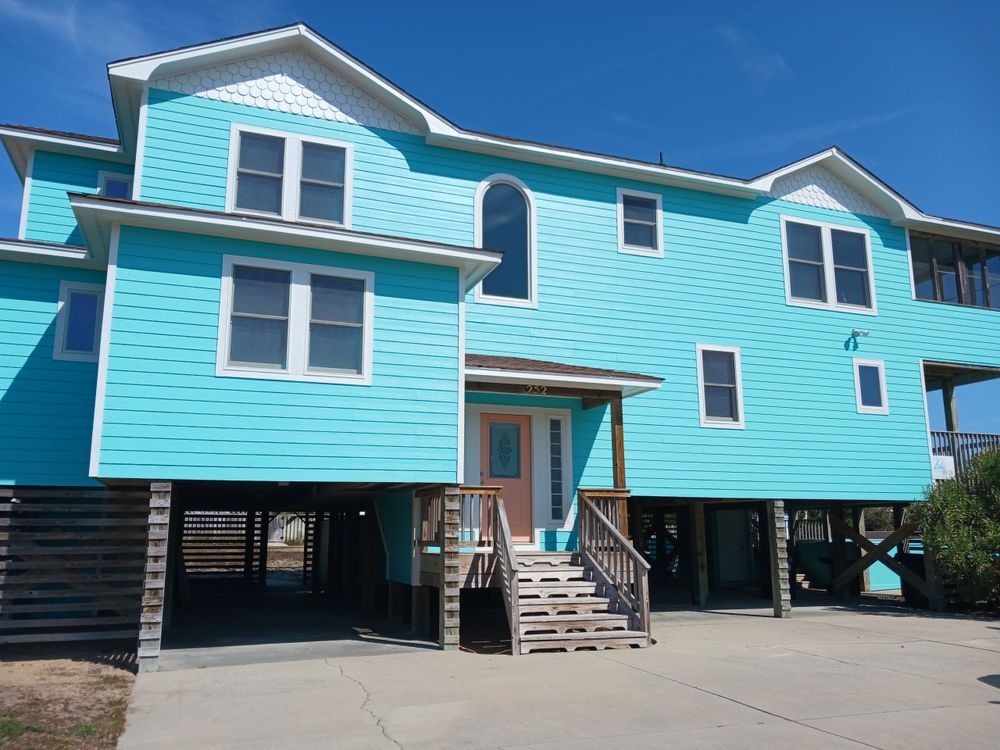Turquoise elevated house on stilts with stairs and parking underneath on a sunny day