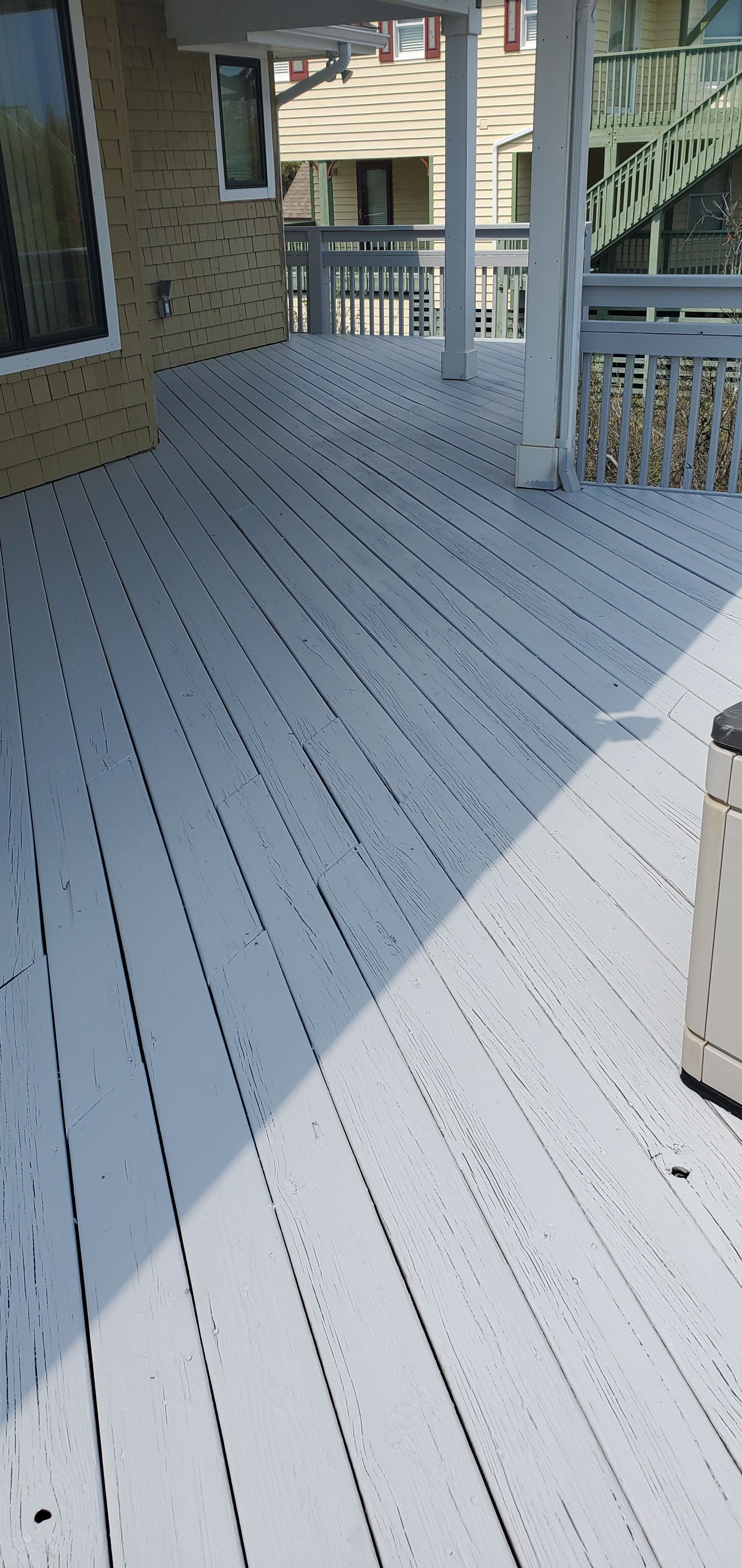 White painted wooden deck or porch with railings beside a brick house, seen in daylight