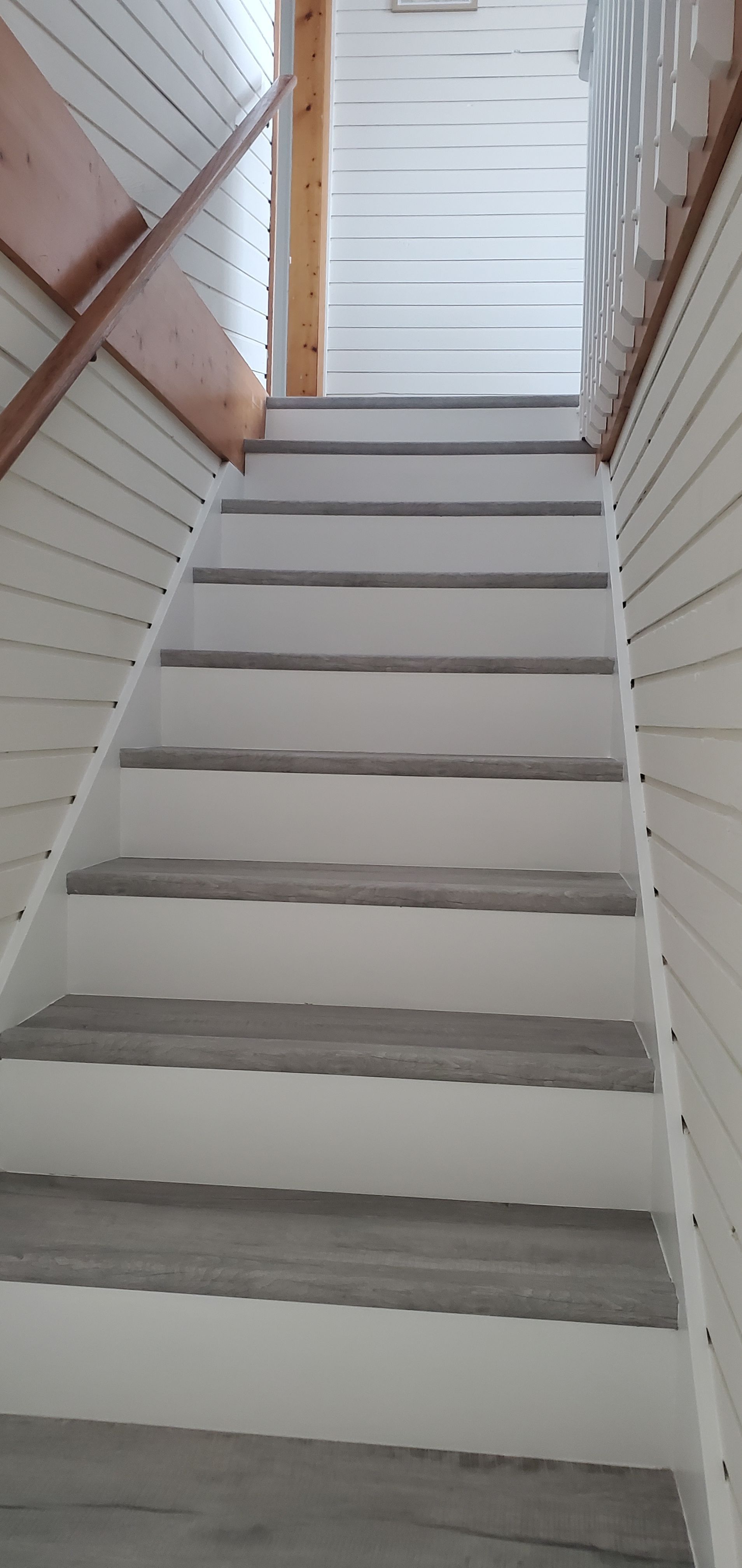 Narrow indoor staircase with white steps and wooden handrails leading up to a doorway