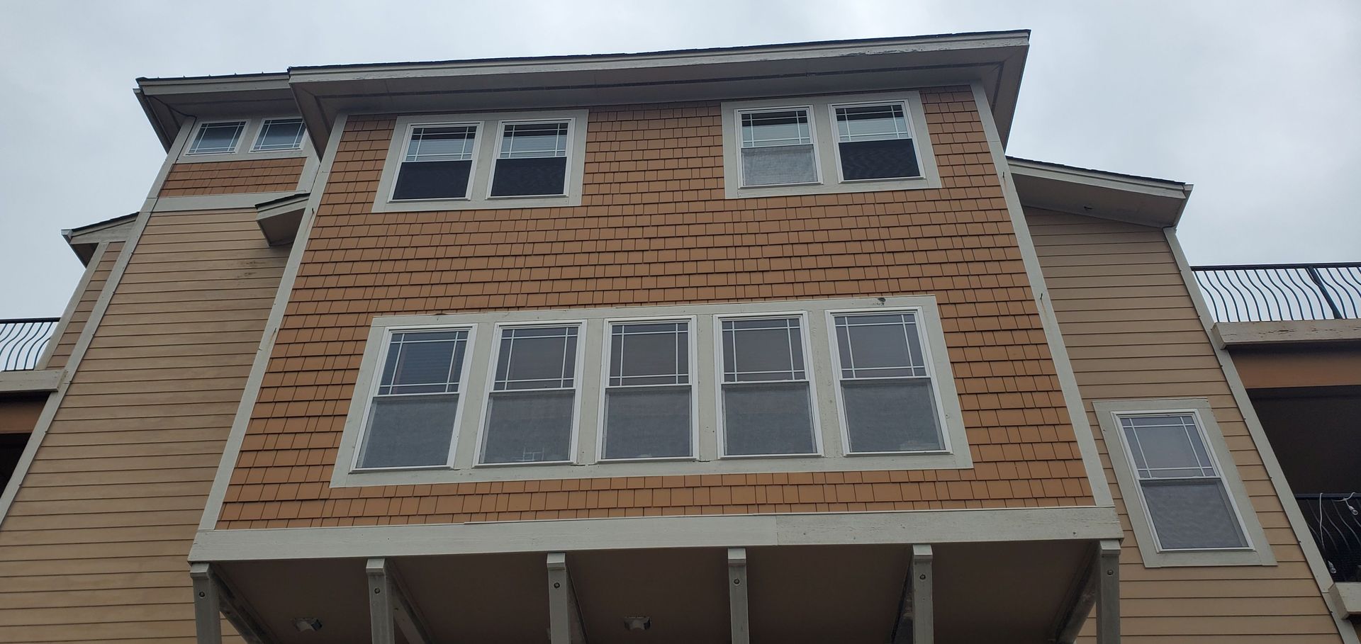 Three-story brick townhouse with white-framed windows and a small balcony under an overcast sky
