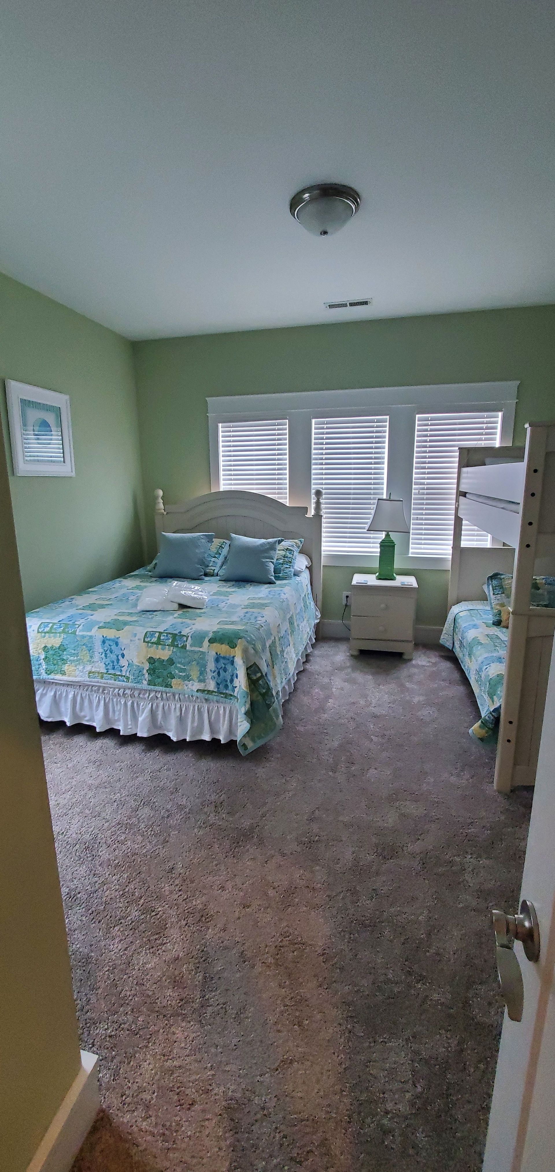 Green bedroom with a bed, nightstand, and window blinds, viewed from the doorway.