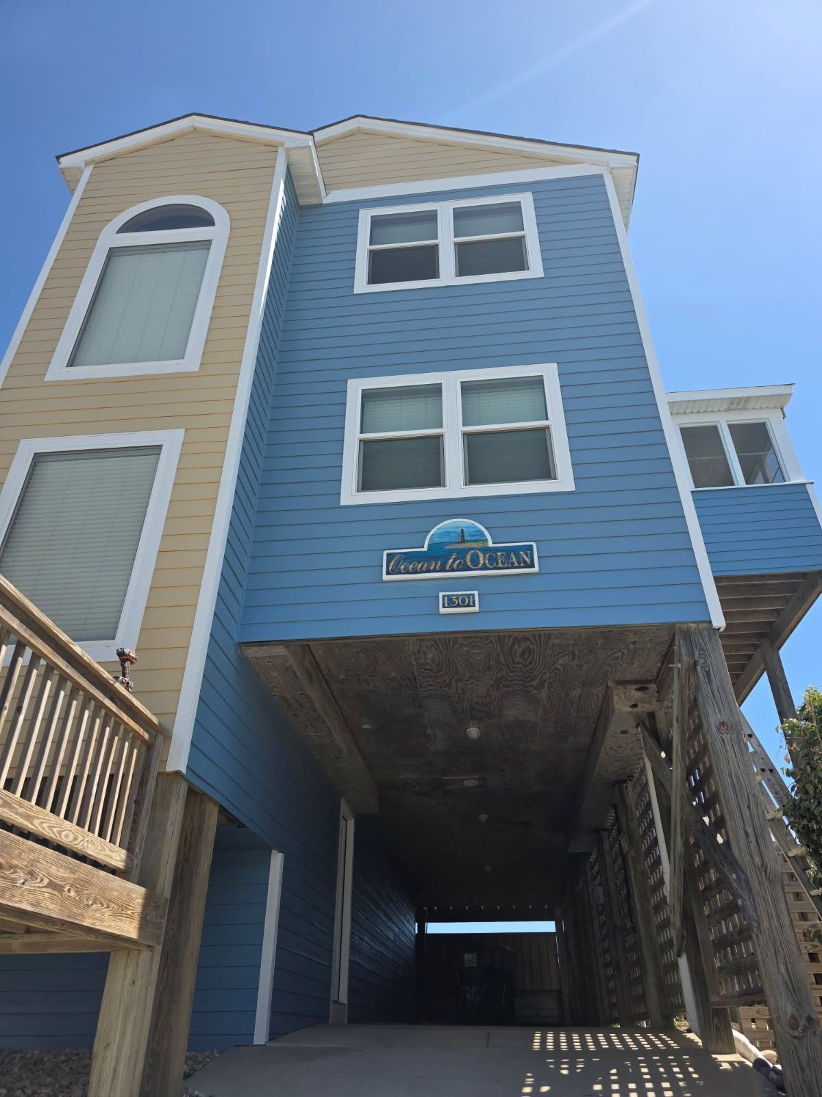 Blue beach house on stilts with white trim, viewed from below against a bright blue sky.