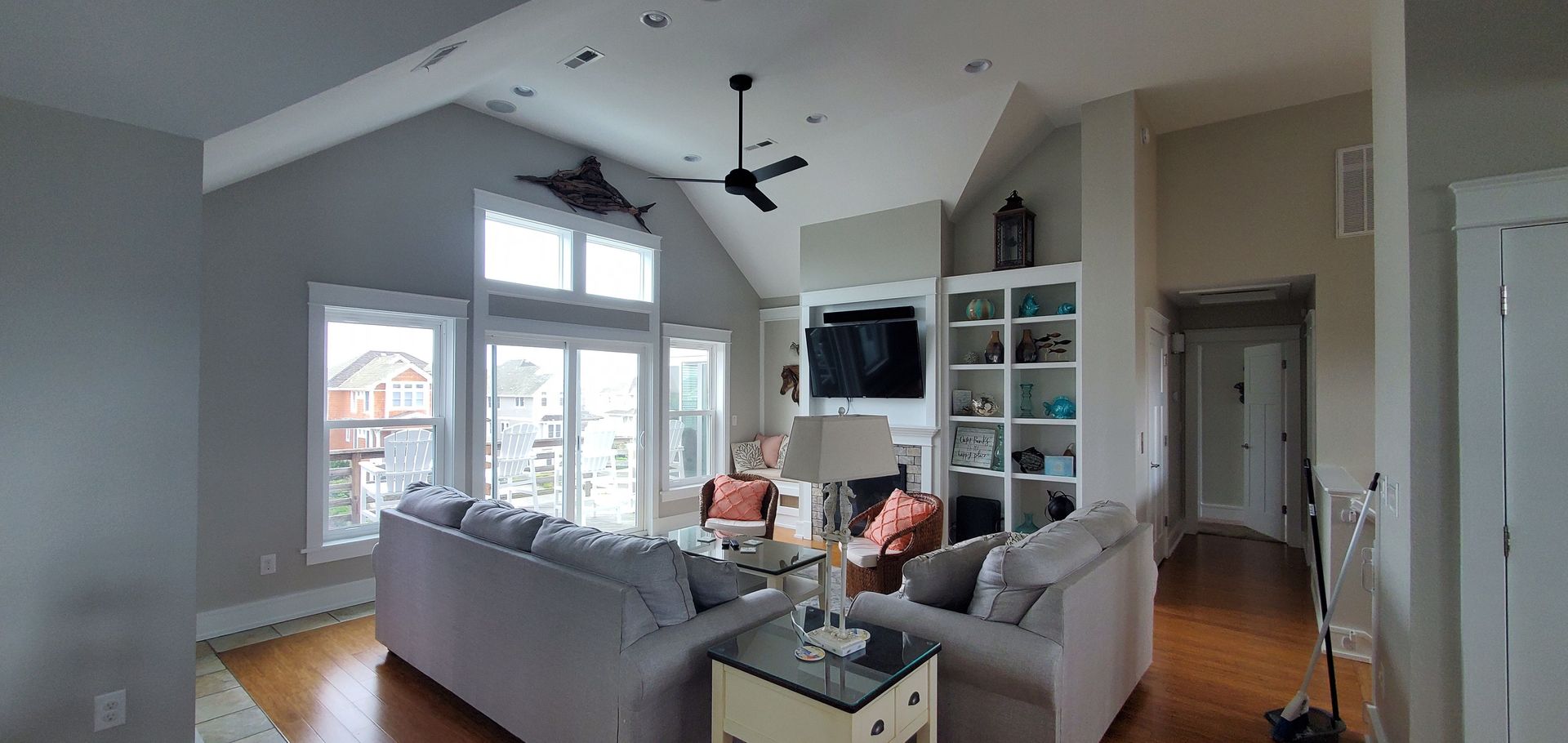 Bright living room with gray sectional, white shelves, hardwood floors, and large windows