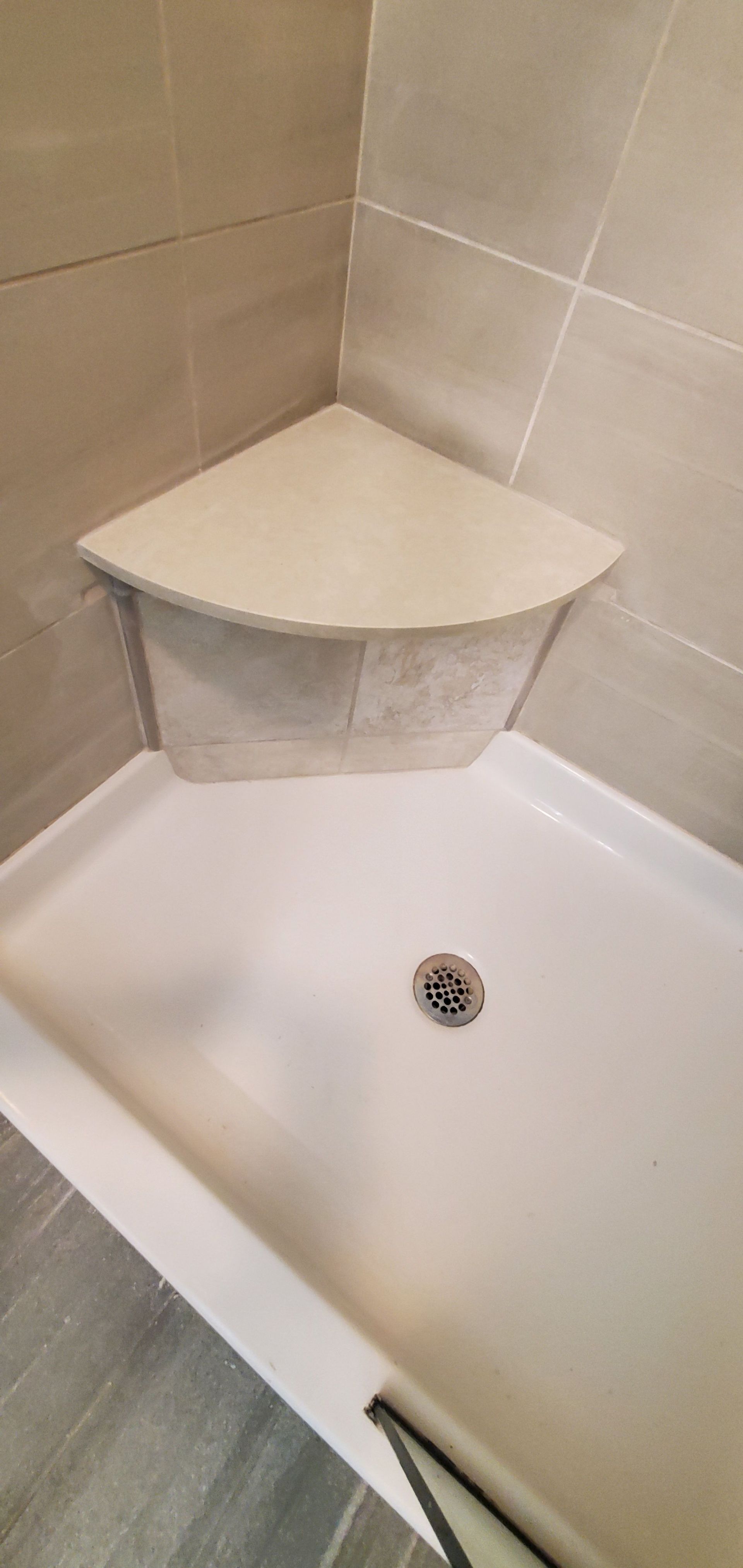 Corner shower with beige tile, white tub, and built-in corner shelf above the drain